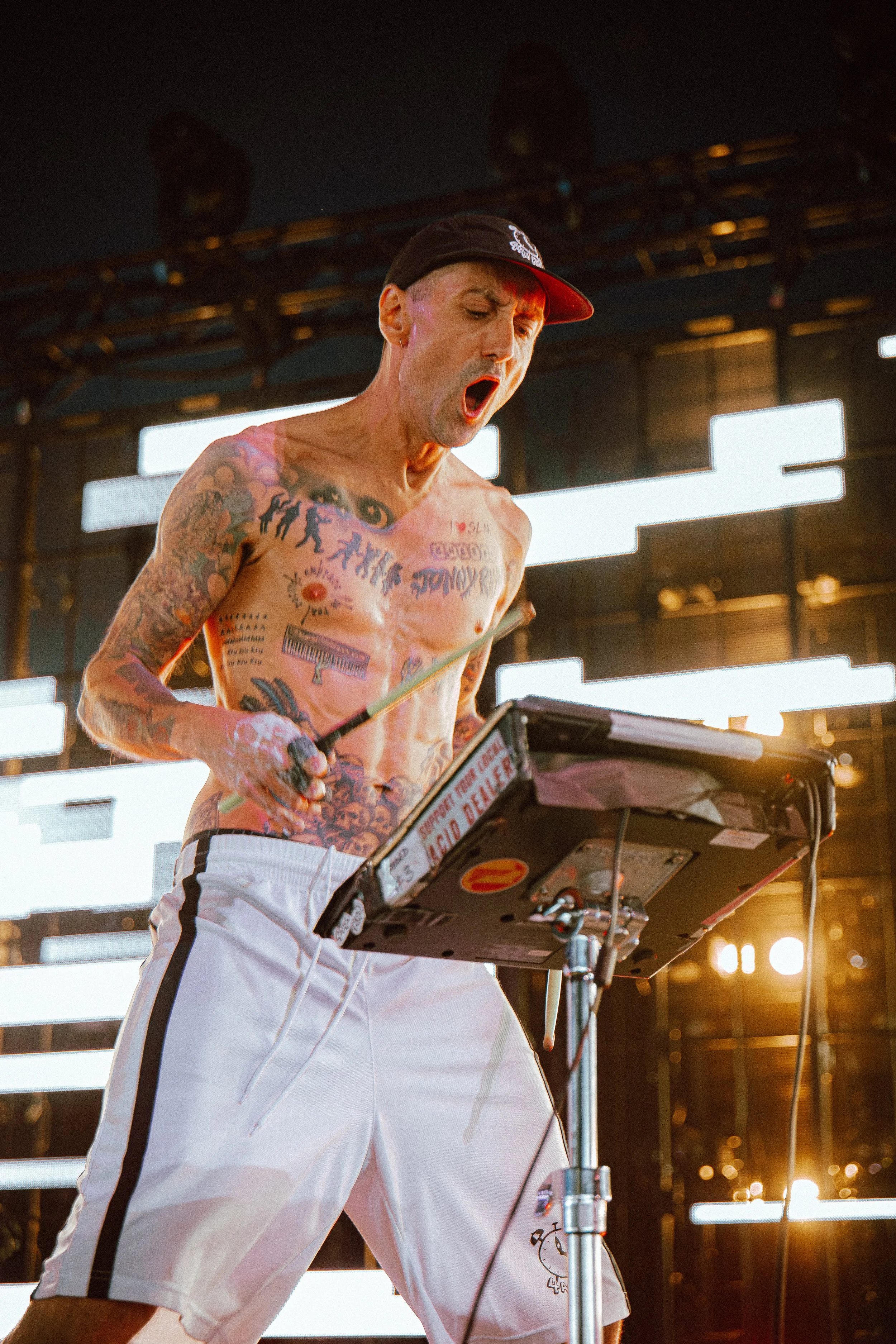 High-energy festival photography of 4am Kru live on stage at Parklife Festival. Close up action shot of the artist performing shirtless with drumsticks. Photo by Will Bailey.
