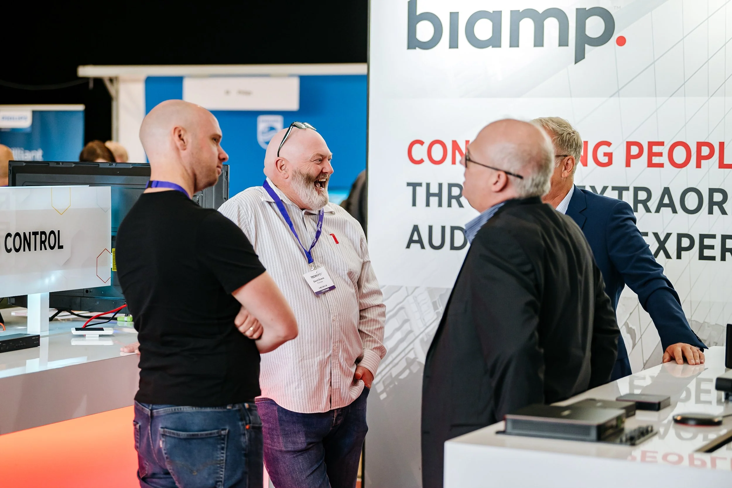 Delegates engaging in a lively business discussion at the Biamp exhibition stand during the Midwich Tech Xpo at Ascot. Professional corporate trade show and tech event photography by Will Bailey.