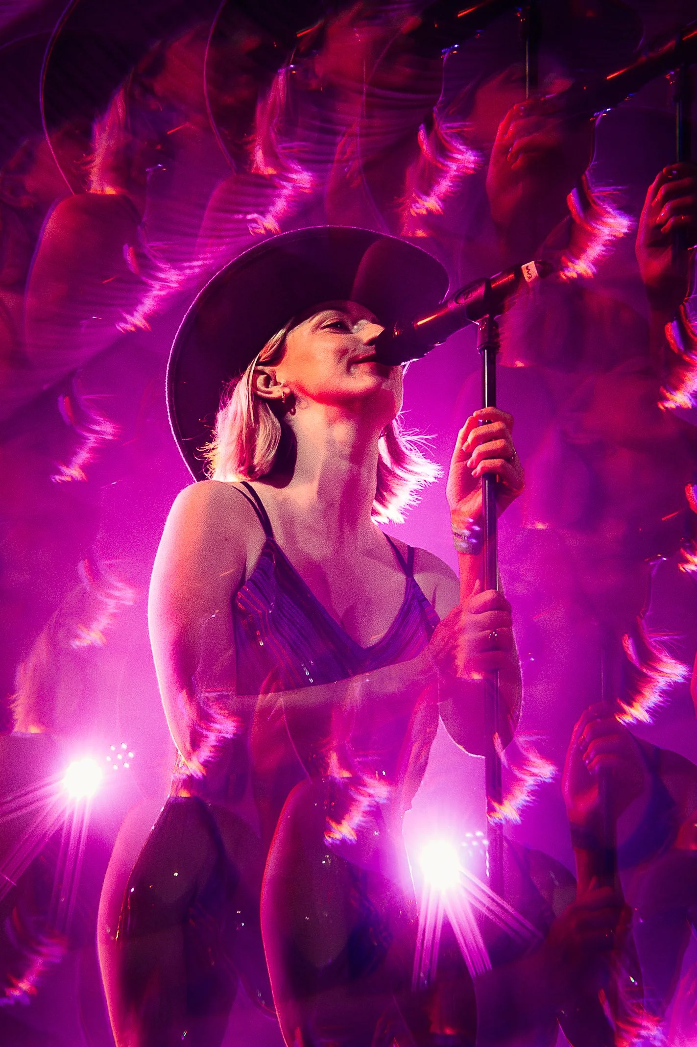 A female country singer in a cowboy hat performing live with the band Made in Tennessee, captured with a creative prism lens effect under vibrant magenta stage lighting by Will Bailey.