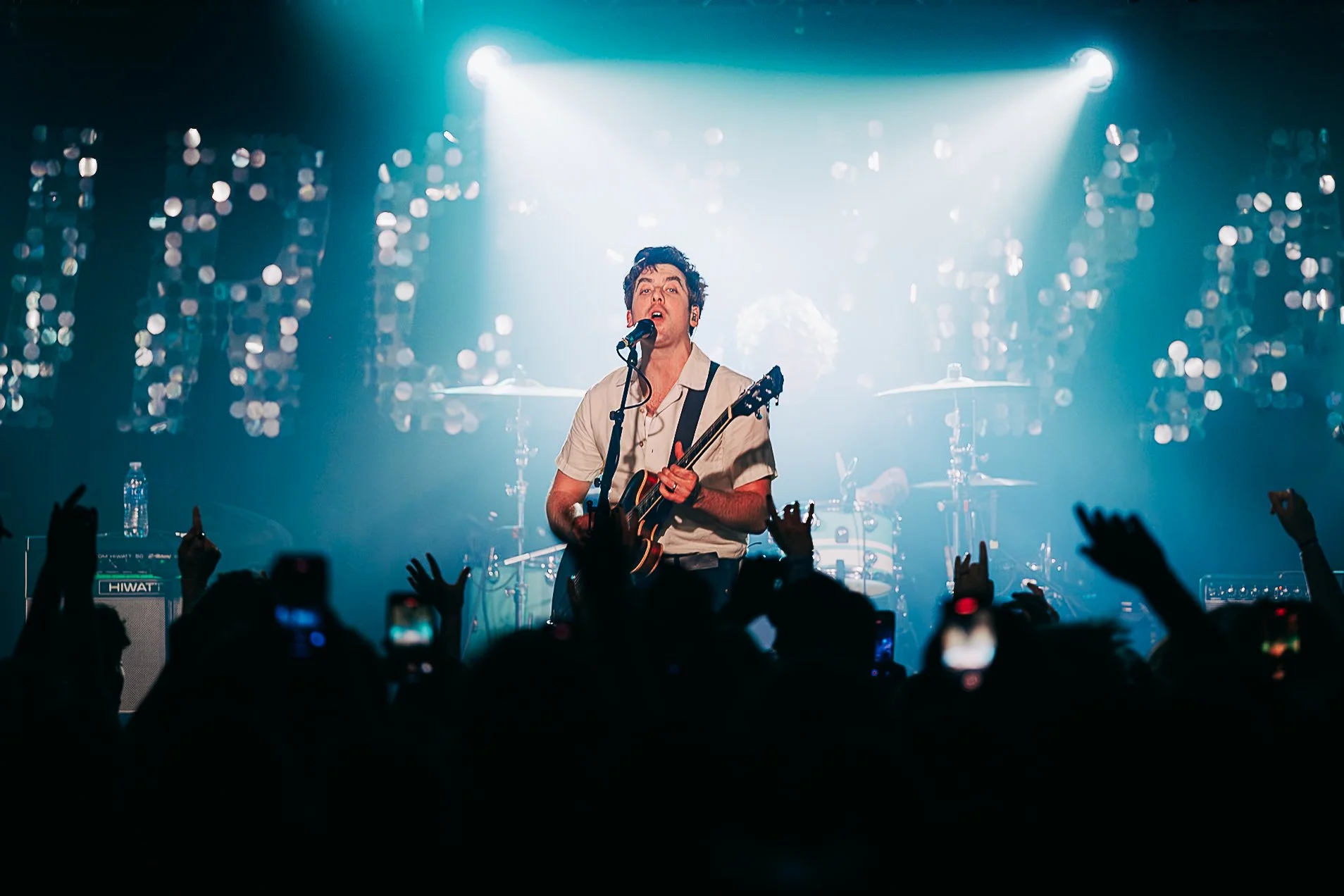 Frontman Kieran Shudall of indie rock band Circa Waves performing on stage at a grassroots venue in Southampton, featuring dynamic teal backlighting and crowd silhouettes by Will Bailey.
