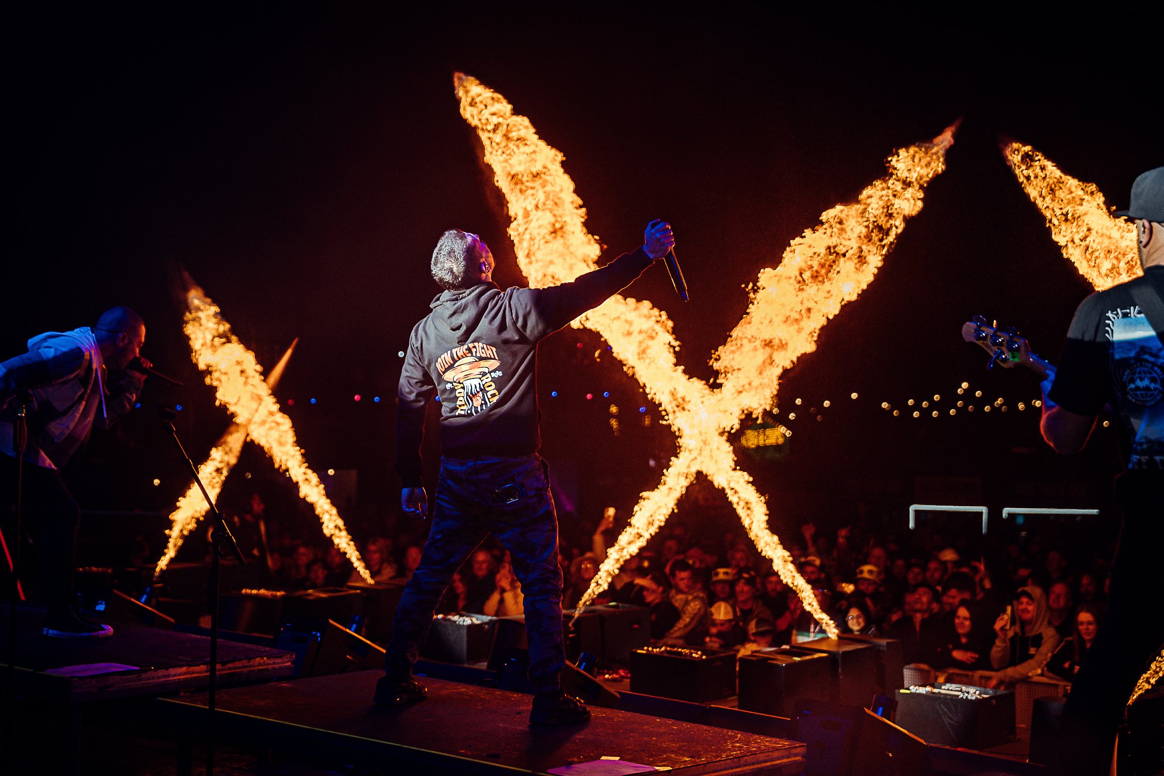 Dramatic festival pyrotechnics photography of a Linkin Park tribute band performing on stage surrounded by giant X-shaped fire flames at Teddy Rocks, shot by Will Bailey.