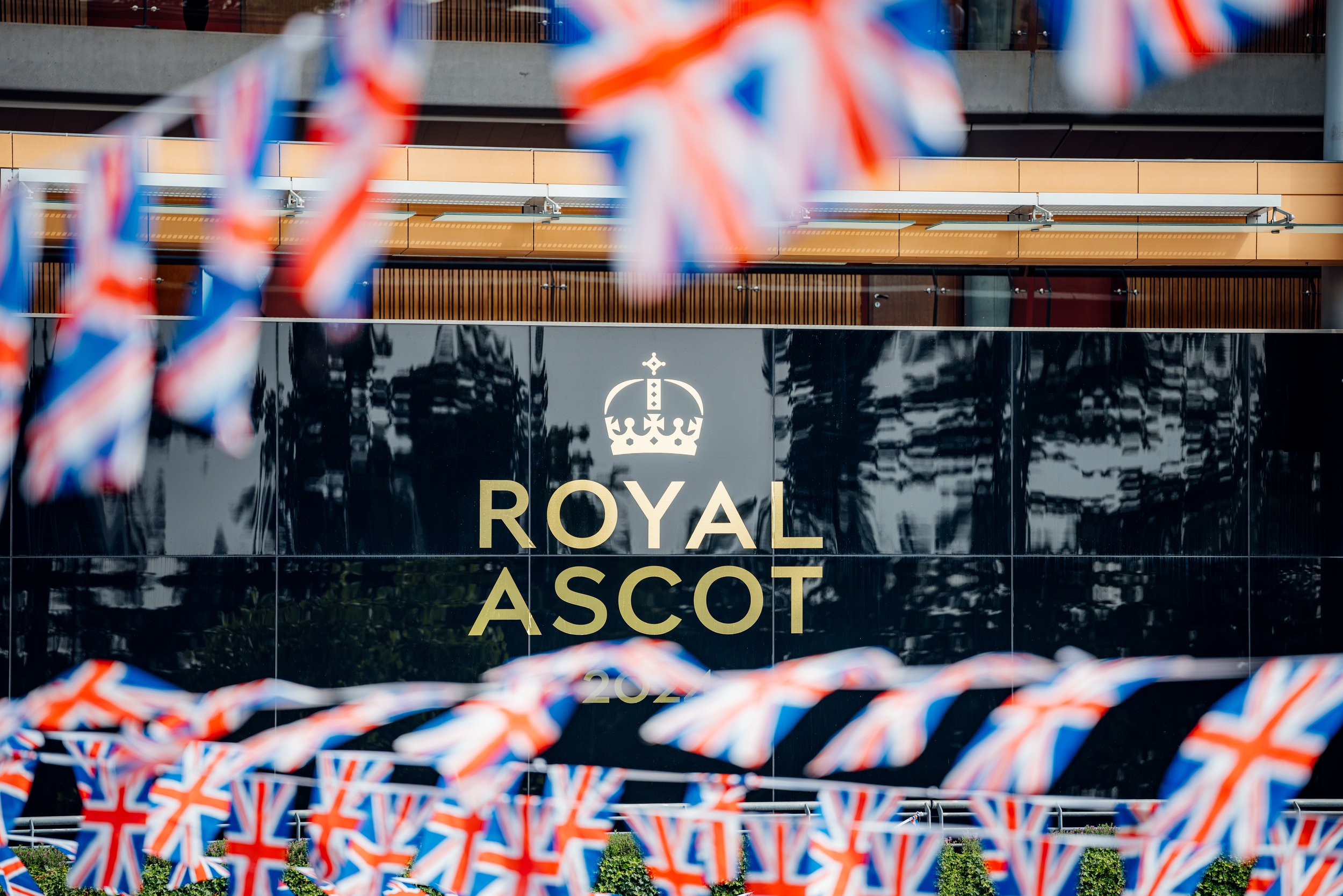 A graphic composition showing the gilded venue branding framed by festive Union Jack bunting at Ascot Racecourse, Berkshire. Luxury sporting venue and British seasonal event tradition photography by Will Bailey.