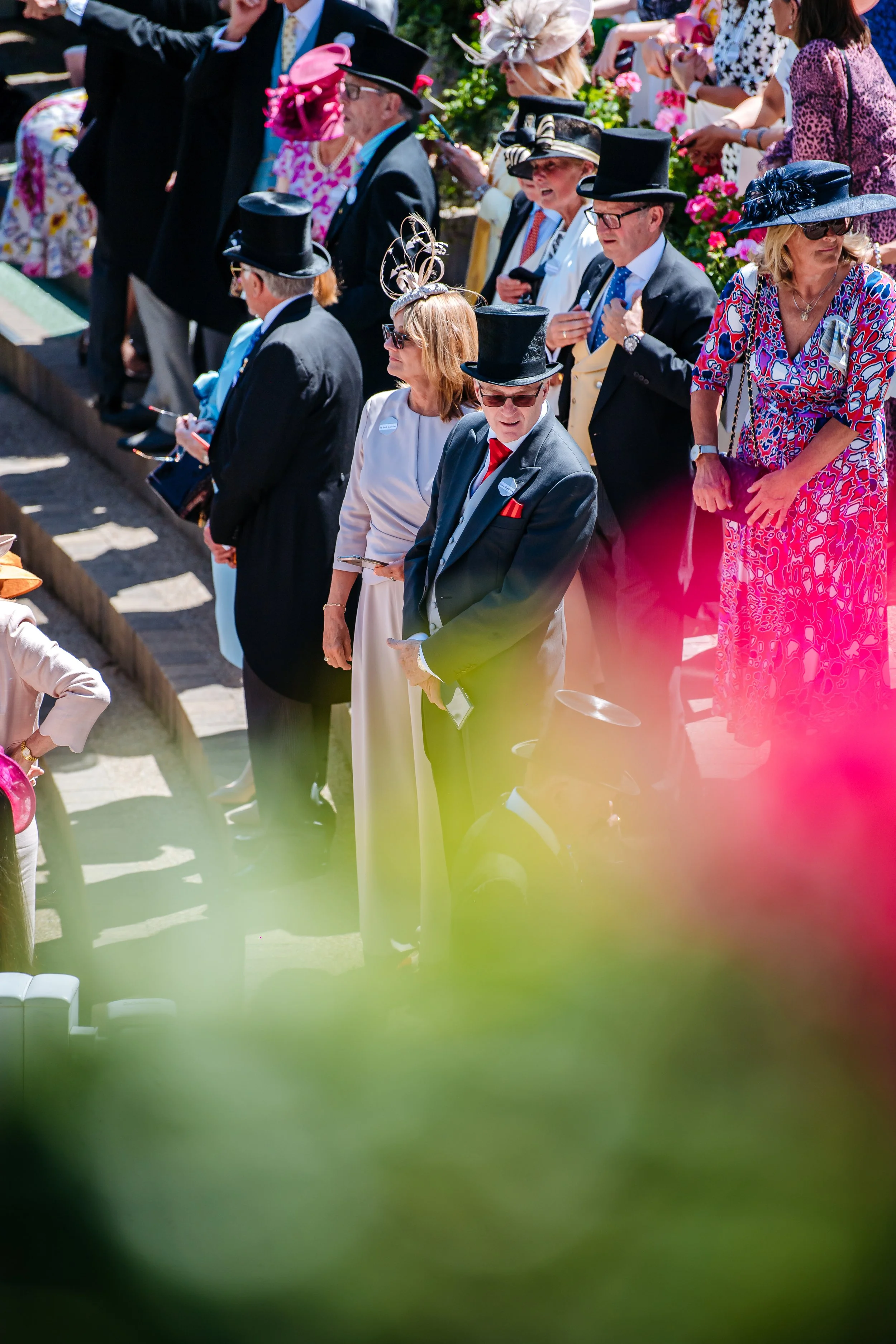 Spectators dressed in traditional morning suits, top hats, and bespoke fascinators watching the races at Royal Ascot. High-society cultural tradition and premium sports event photography by Will Bailey.