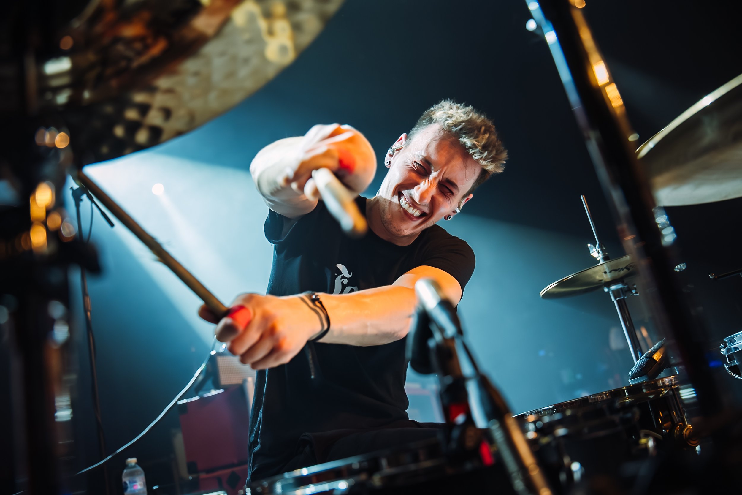 A dramatic close-up capturing the raw intensity of drummer, Matt Bicker, of the pop-punk band The Bottom Line performing live at the UEA LCR venue in Norwich. On-the-road tour documentary and live band photography by official tour photographer Will B