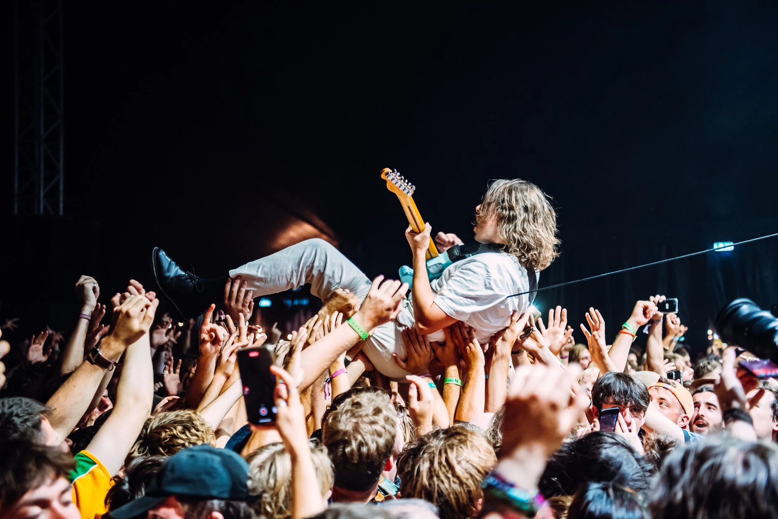 A guitarist from punk rock band IDLES crowd-surfs over a sea of fans while playing a solo live at Boardmasters in Cornwall. Dynamic music festival crowd interaction and high-action stage performance photography by Will Bailey.