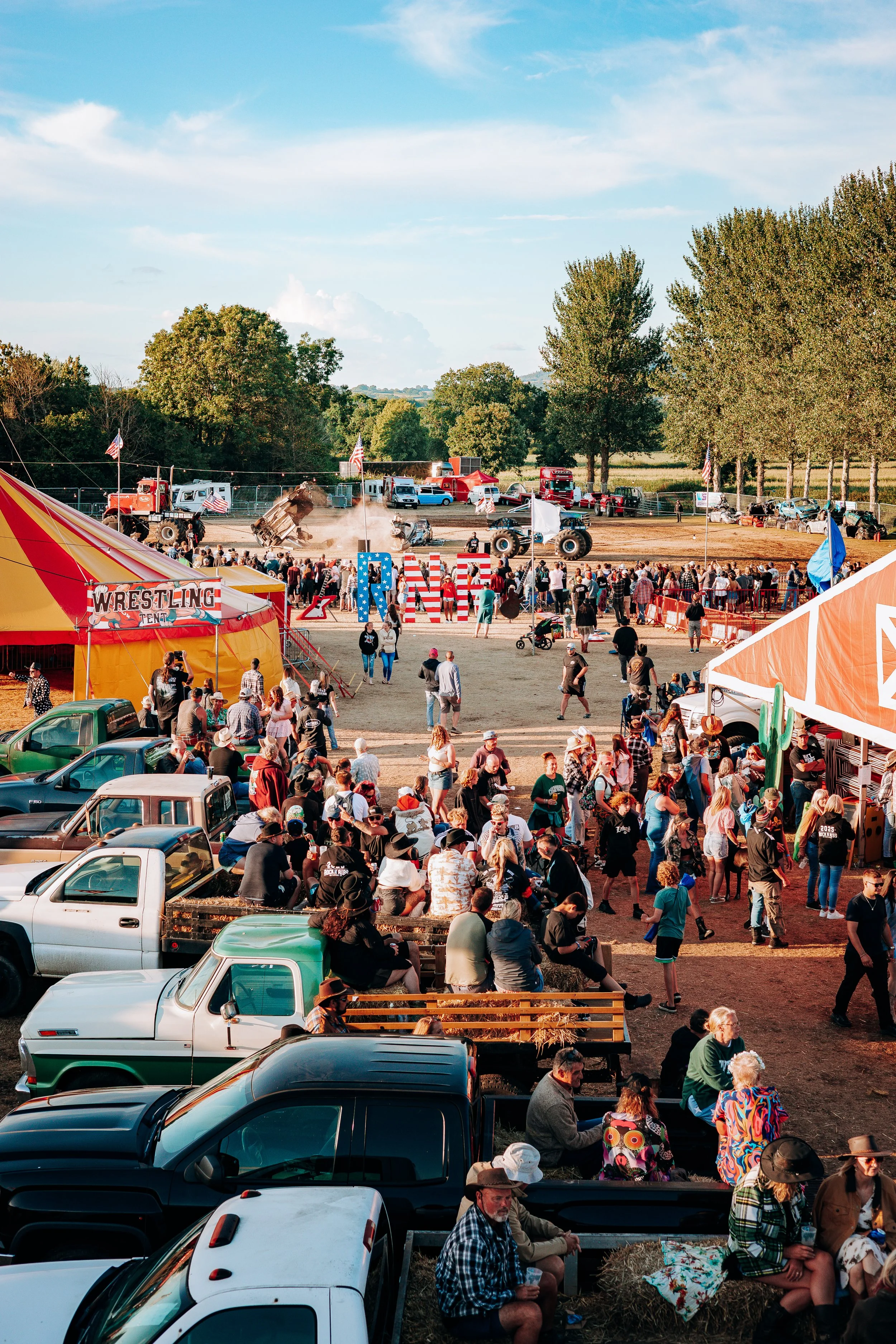 An elevated view looking down a line of tailgating trucks through to the monster truck stunt arena at the Rock n Ribs Festival. American-style public festival culture and high-action event photography by Will Bailey.