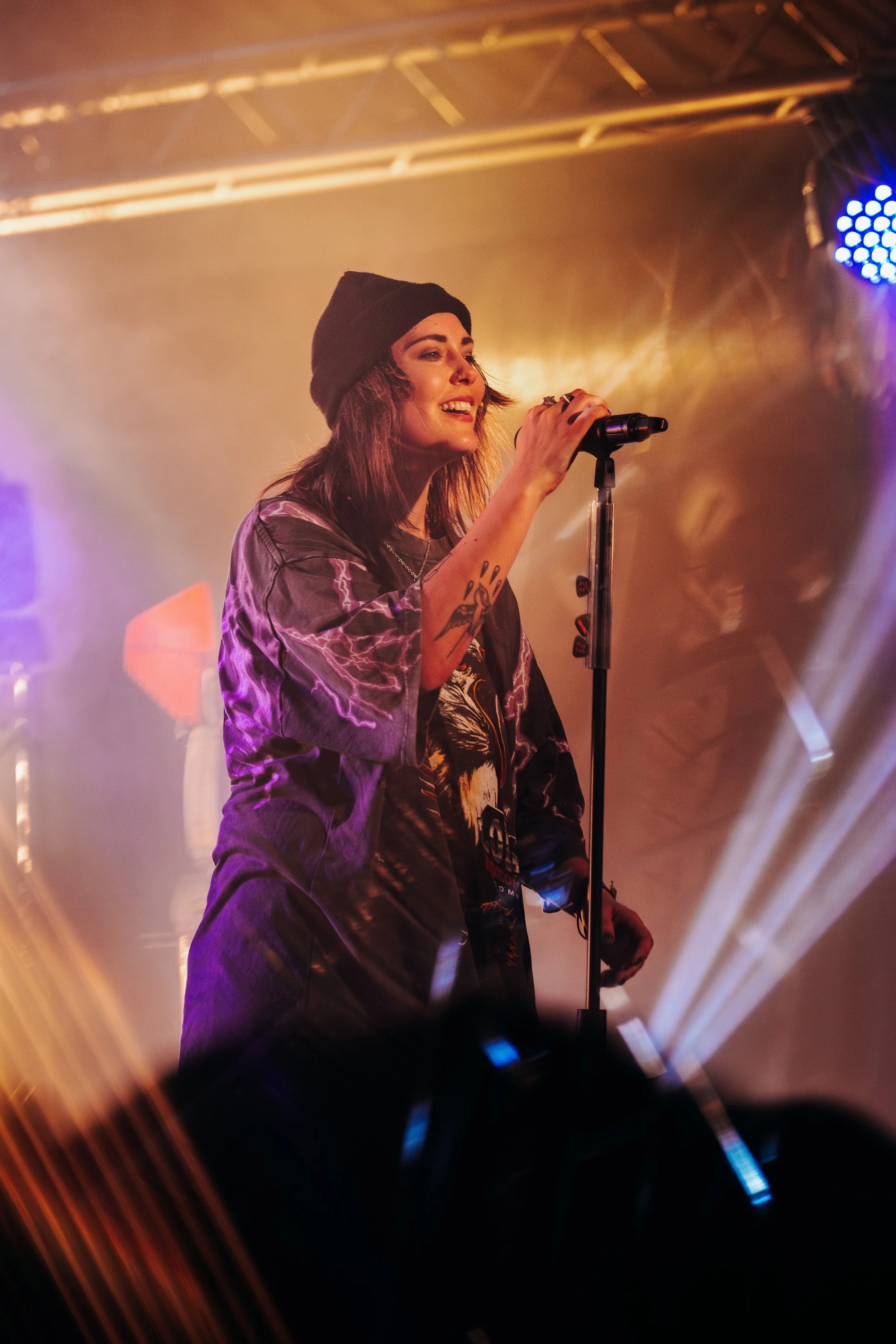 Lead vocalist Bonnie Fraser of Stand Atlantic singing into a spotlight while wearing a beanie at a popular live music venue in Southampton. High-energy alternative rock concert and professional touring band photography by Will Bailey.