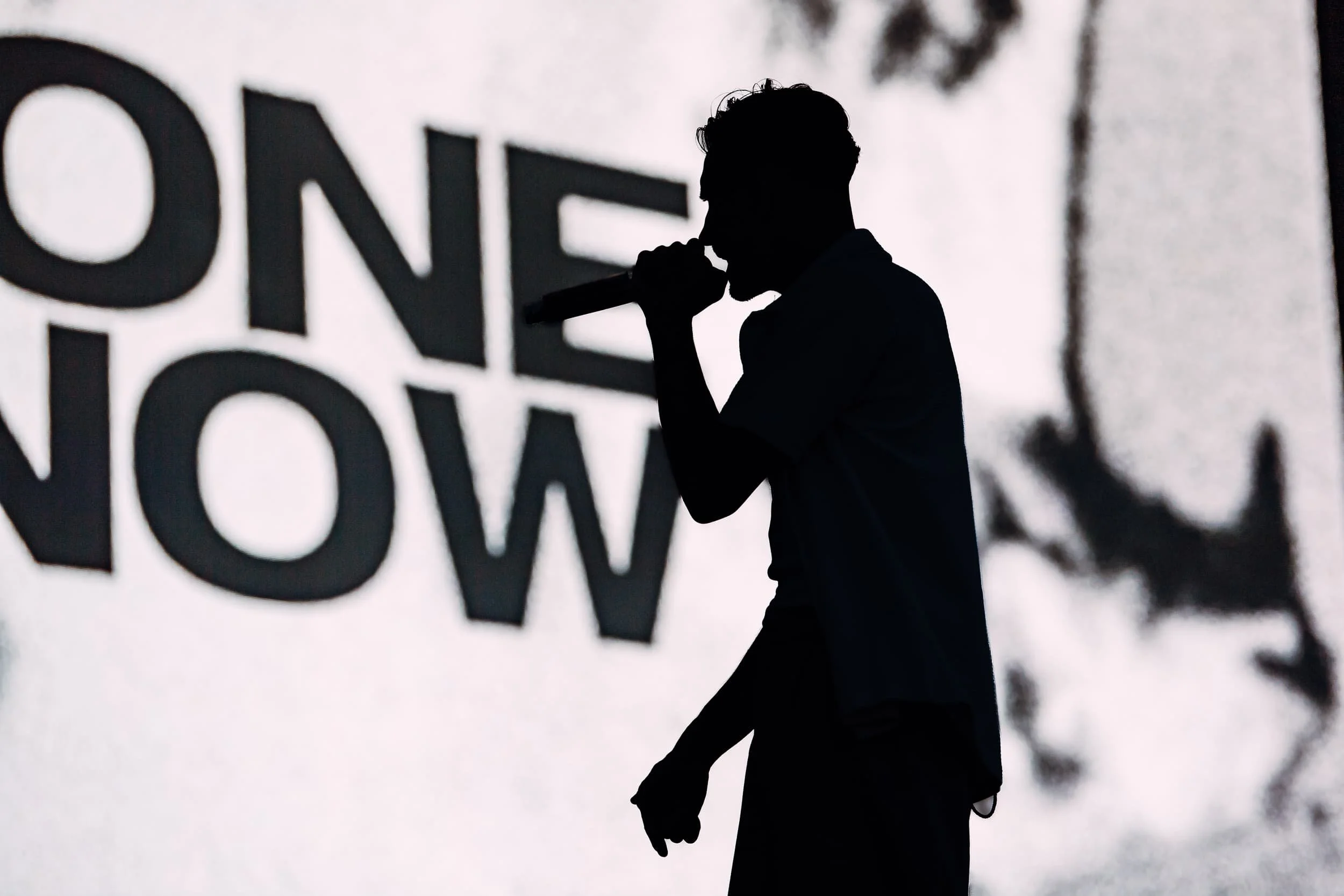 Editorial silhouette photography of Everyone You Know live at Boardmasters Festival. Side profile shot of artist singing into a microphone. Photo by Will Bailey.