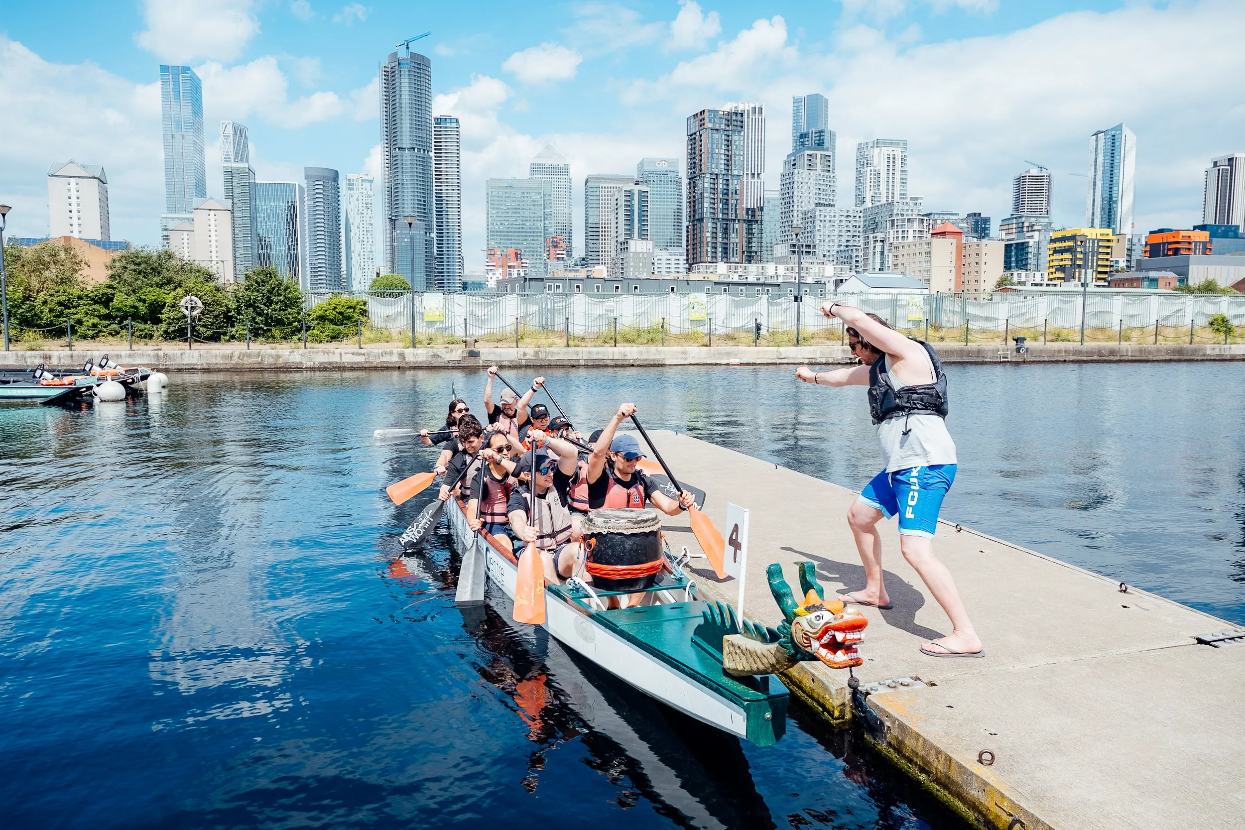 A team hitting the water in their dragon boat as their drummer sets the pace during the Far East Consortium (FEC) Charity Dragon Boat Festival, with the iconic Canary Wharf and London Docklands skyline in the background. Corporate charity regatta and