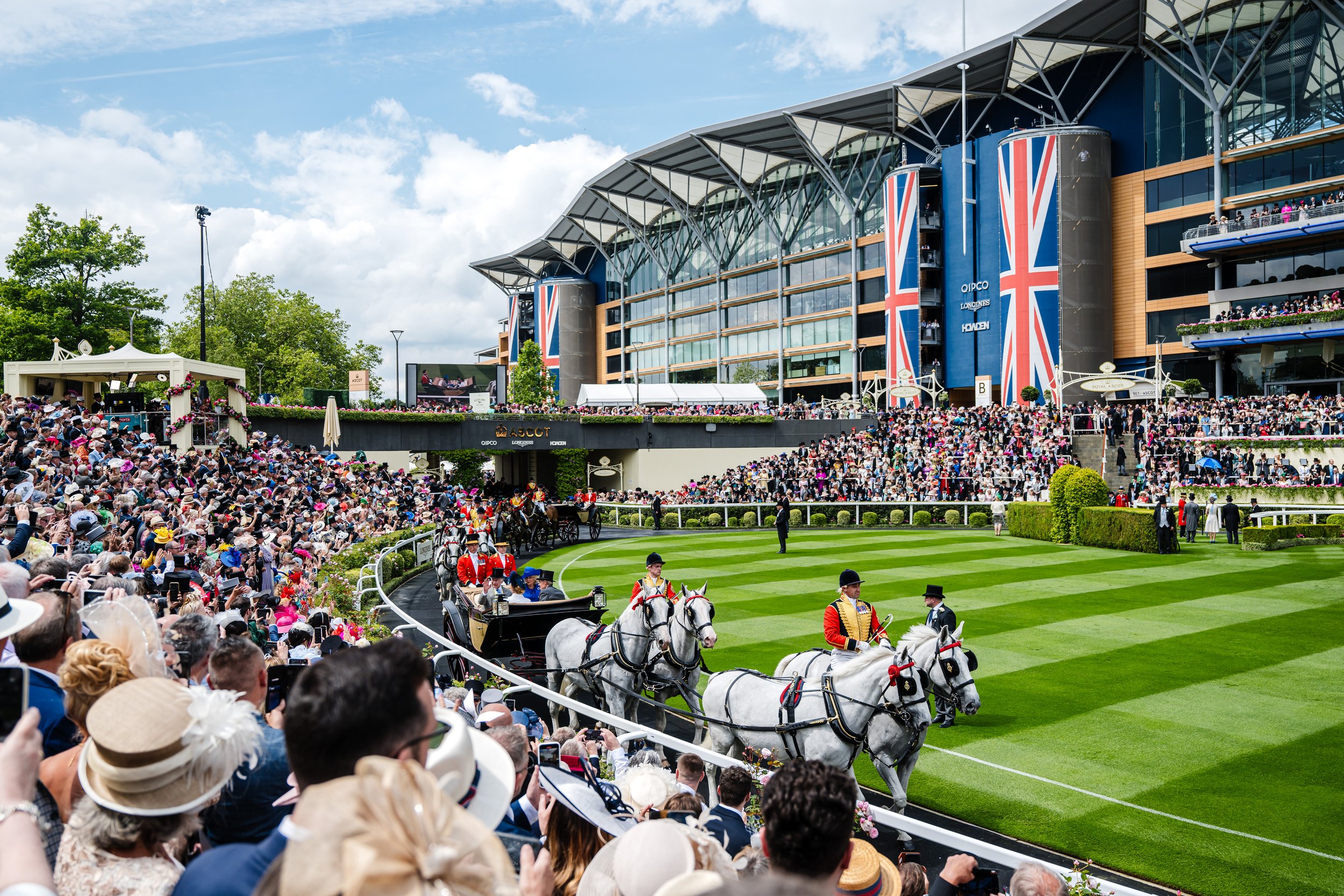 The Royal Procession carriages entering the parade ring in front of packed grandstands during the summer race meeting at Royal Ascot, Berkshire. Prestigious cultural event and historic British lifestyle photography by Will Bailey.