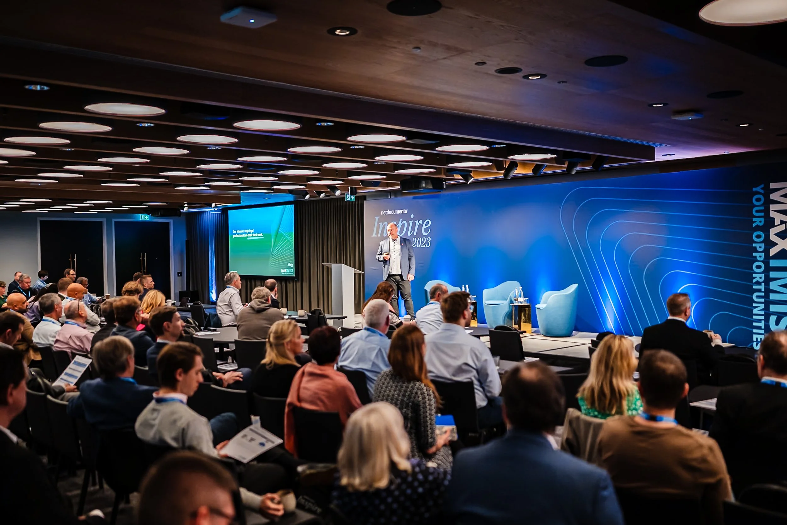 A wide-angle view of a keynote speaker presenting on stage to a full audience during the NetDocuments Inspire conference at Convene 22 Bishopsgate, London. Corporate summit and conference photography by Will Bailey.