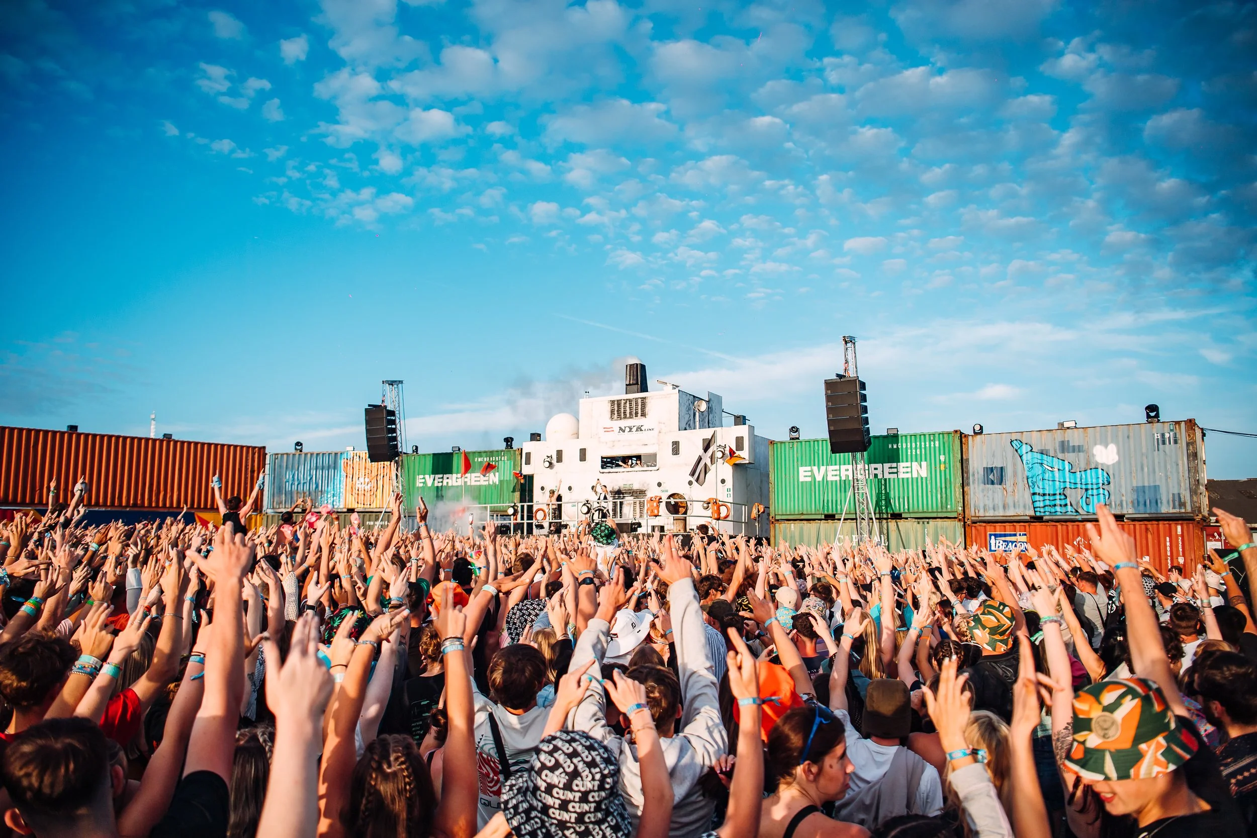 Daytime festival crowd photography capturing thousands of arms raised at the shipping container DB90 stage during Boardmasters Festival in Cornwall, by festival photographer Will Bailey.