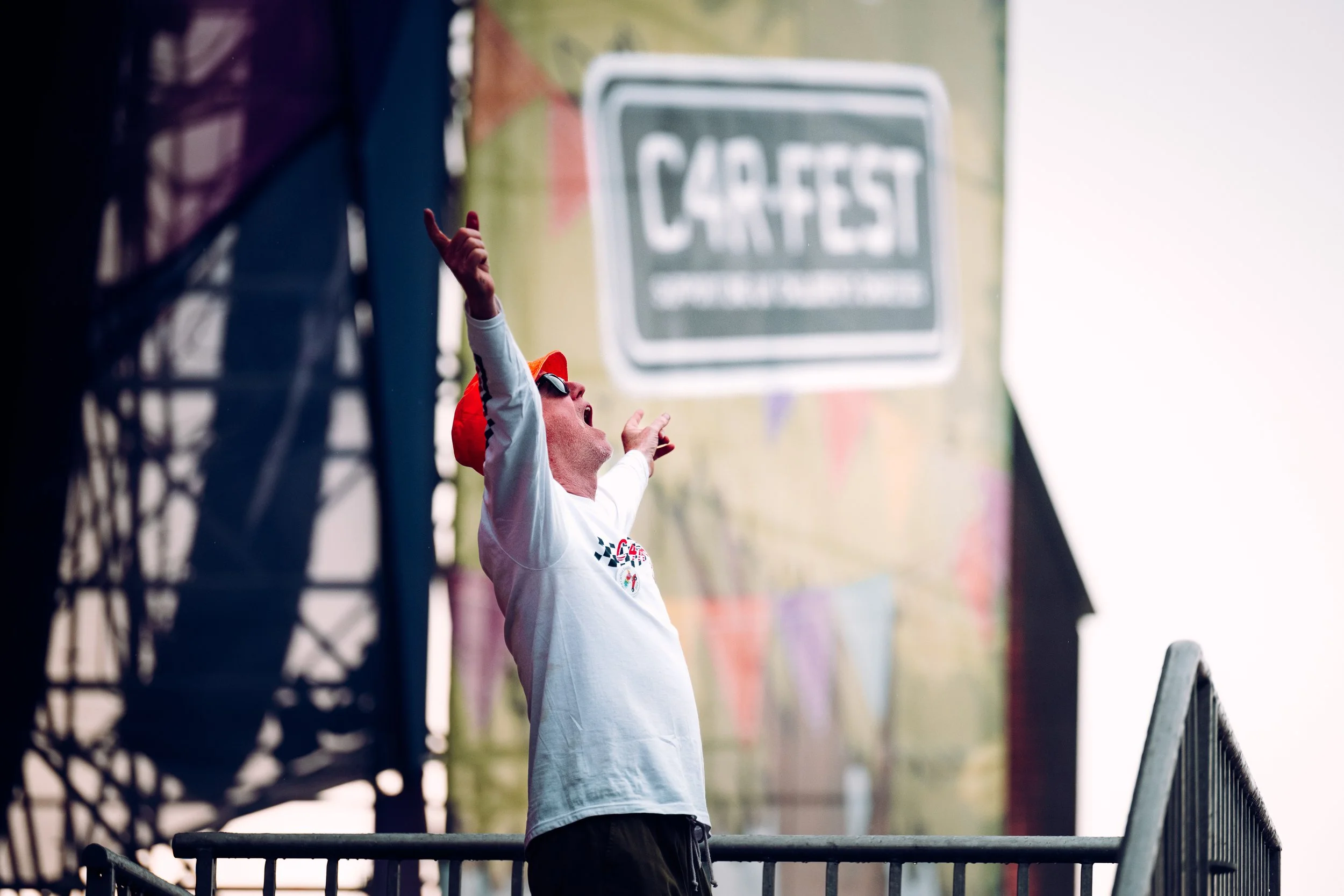 Broadcaster and festival founder Chris Evans energises the main stage crowd from the gantry rails during a summer weekend session at CarFest. High-profile celebrity hosting and large-scale charity festival photography by Will Bailey.