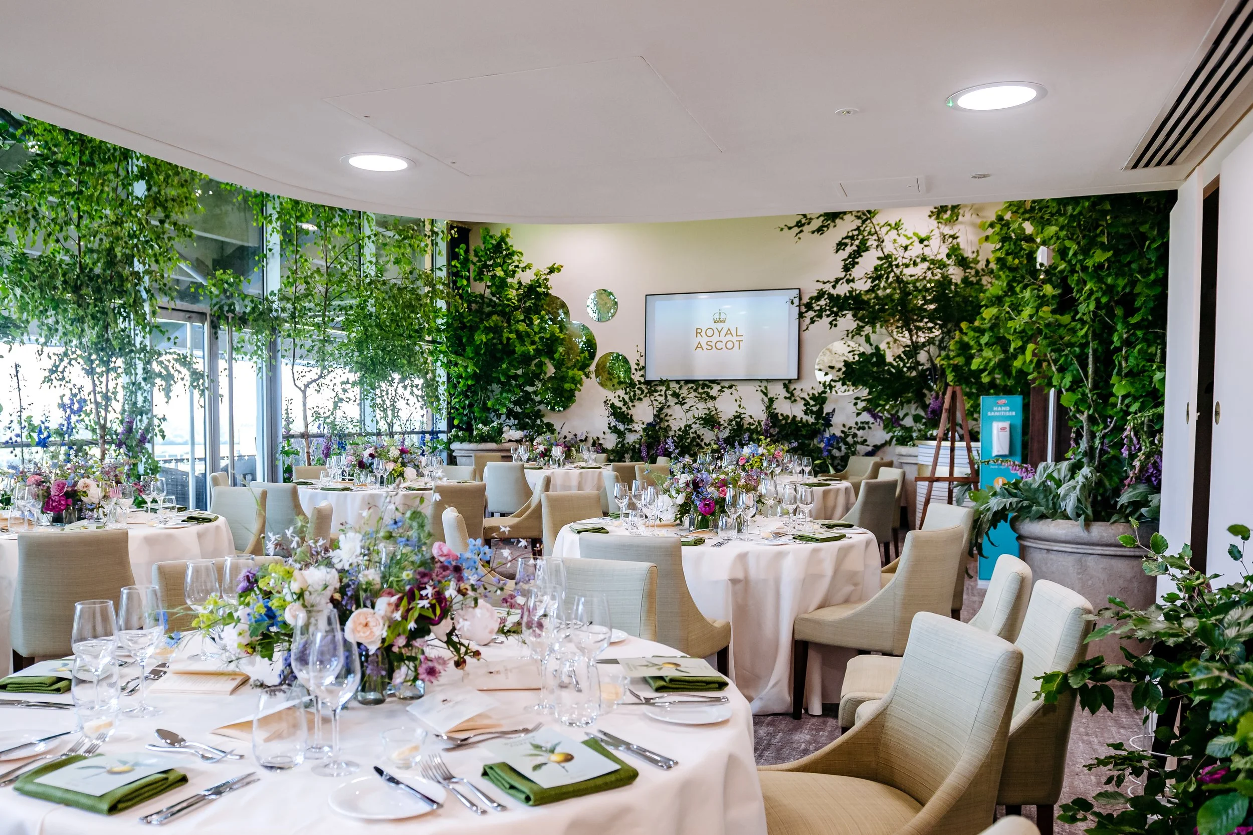Bespoke floral centerpieces and pristine tableware layouts inside an elegant pop-up dining suite at Royal Ascot. Luxury event design, hospitality catering, and venue interior photography by Will Bailey.