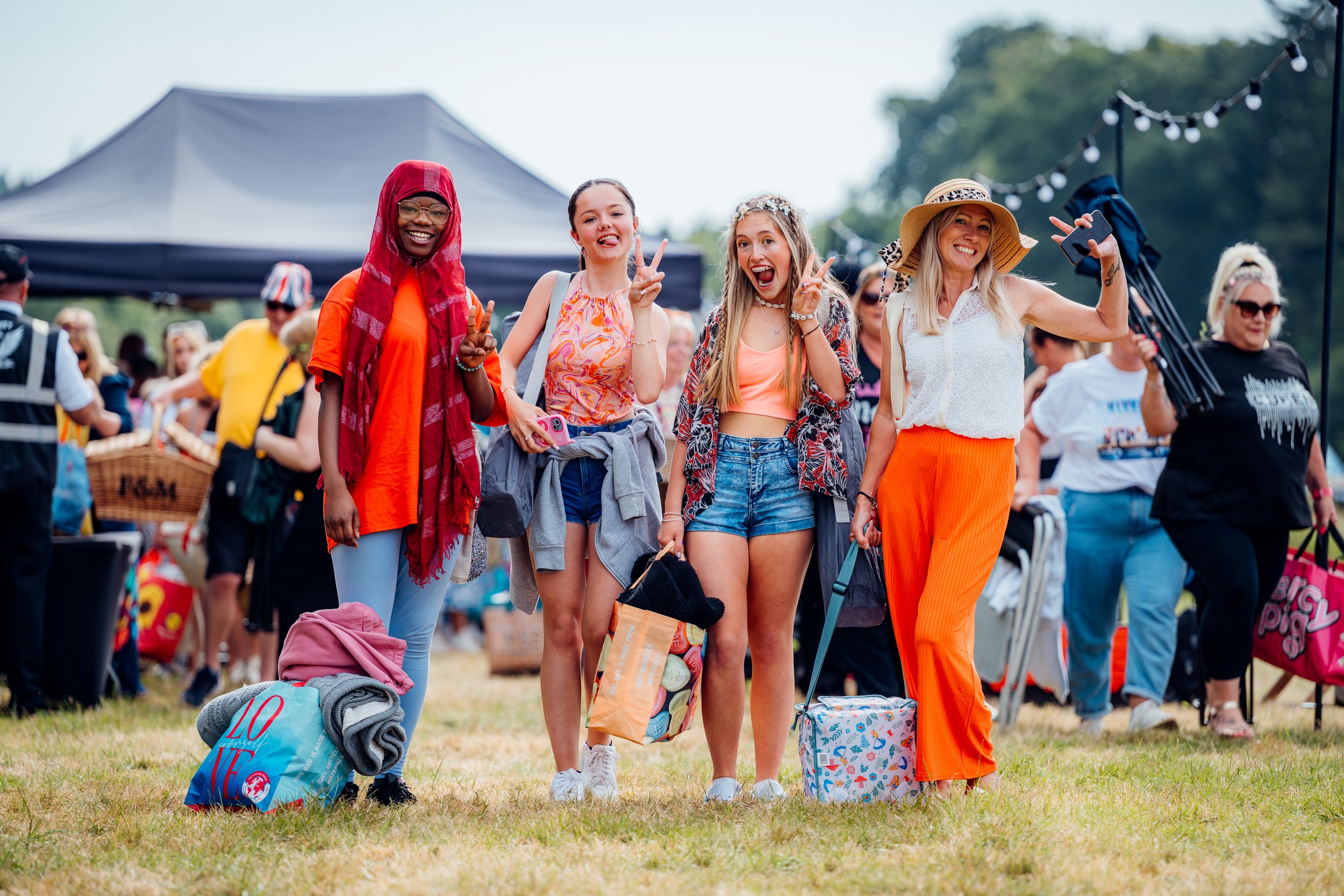 A group of friends carrying picnic blankets and gear as they arrive for an outdoor cinema screening event in Hampshire. Candid public lifestyle and experiential summer festival photography by Will Bailey.