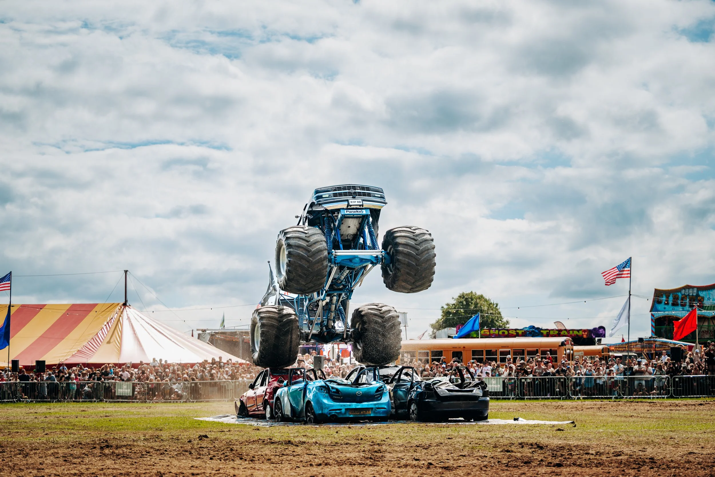 A monster truck leaping into the air to crush vehicles in front of a packed crowd at the Rock n Ribs Festival. High-action public entertainment and summer festival photography by Will Bailey.