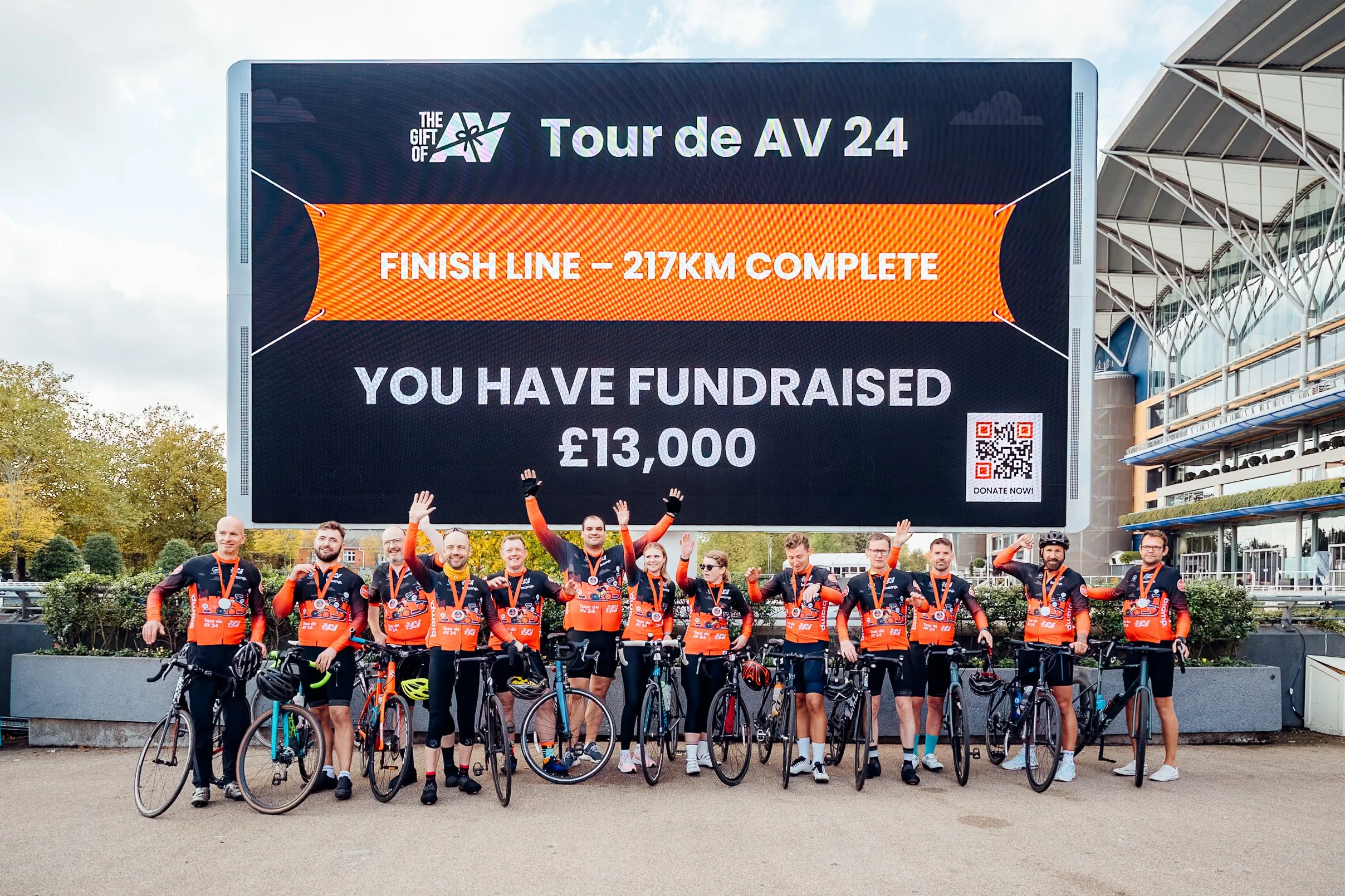The "Tour de AV 24" charity cyclists celebrating at the Ascot finish line during the Midwich Tech Xpo. Corporate social responsibility (CSR) and event photography by Will Bailey.
