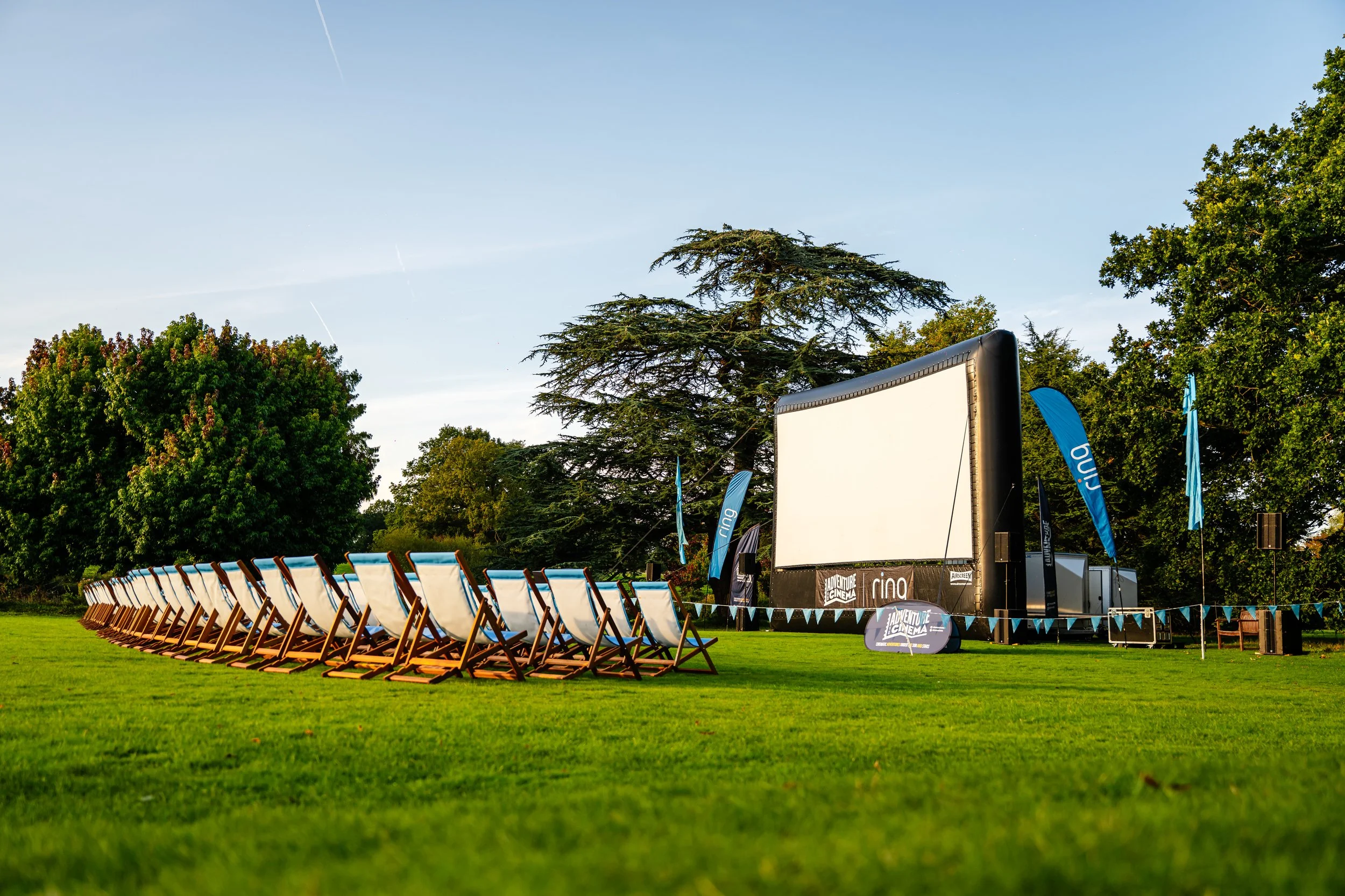 A crisp view of a giant inflatable movie screen framed by structured deckchairs on the lawn at The Vyne in Basingstoke, Hampshire. Premium open-air cinema and National Trust venue event photography by Will Bailey.