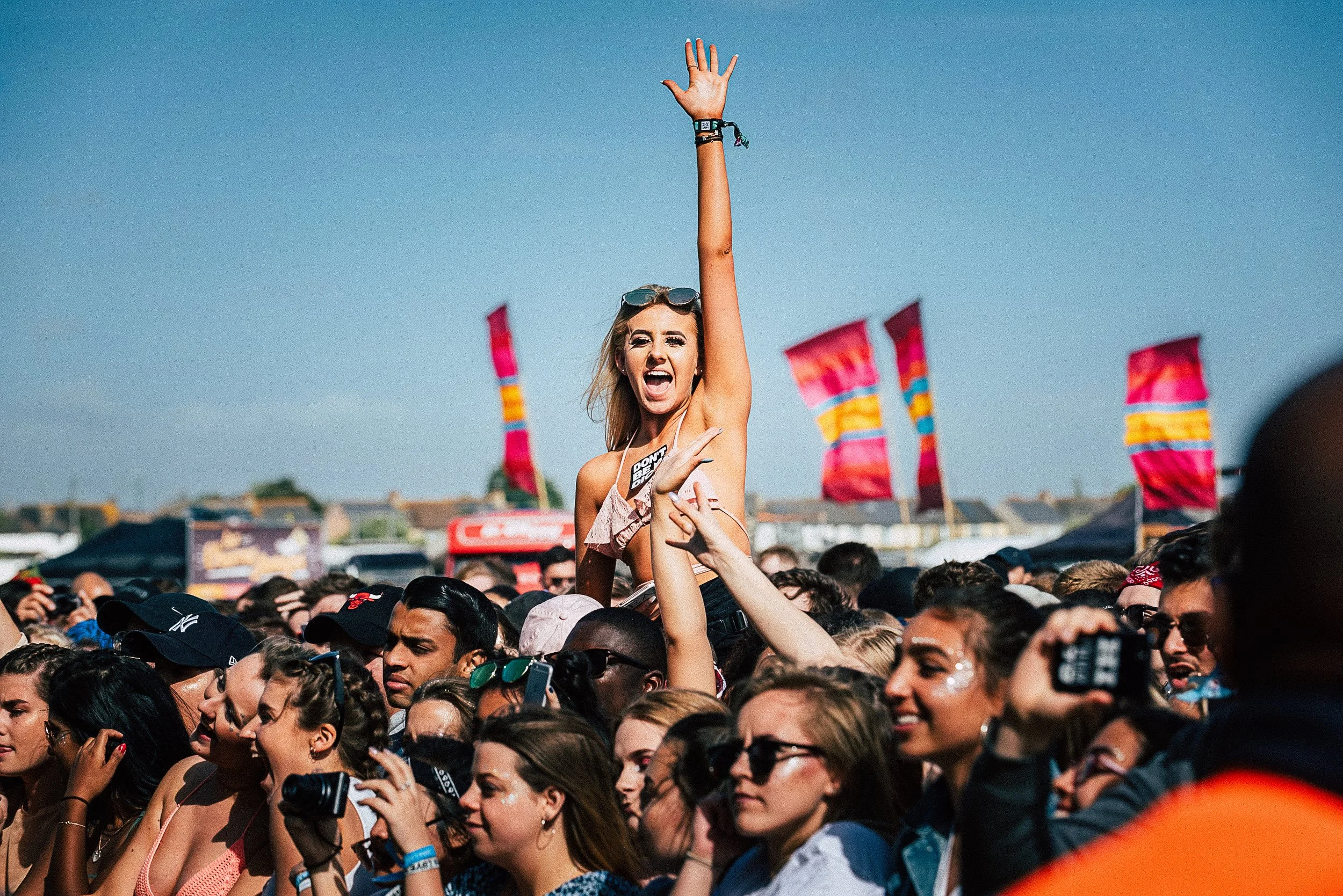 High-energy festival crowd photography of a girl cheering on shoulders at the barrier during WILD LIFE Festival in Brighton, shot by music photographer Will Bailey.
