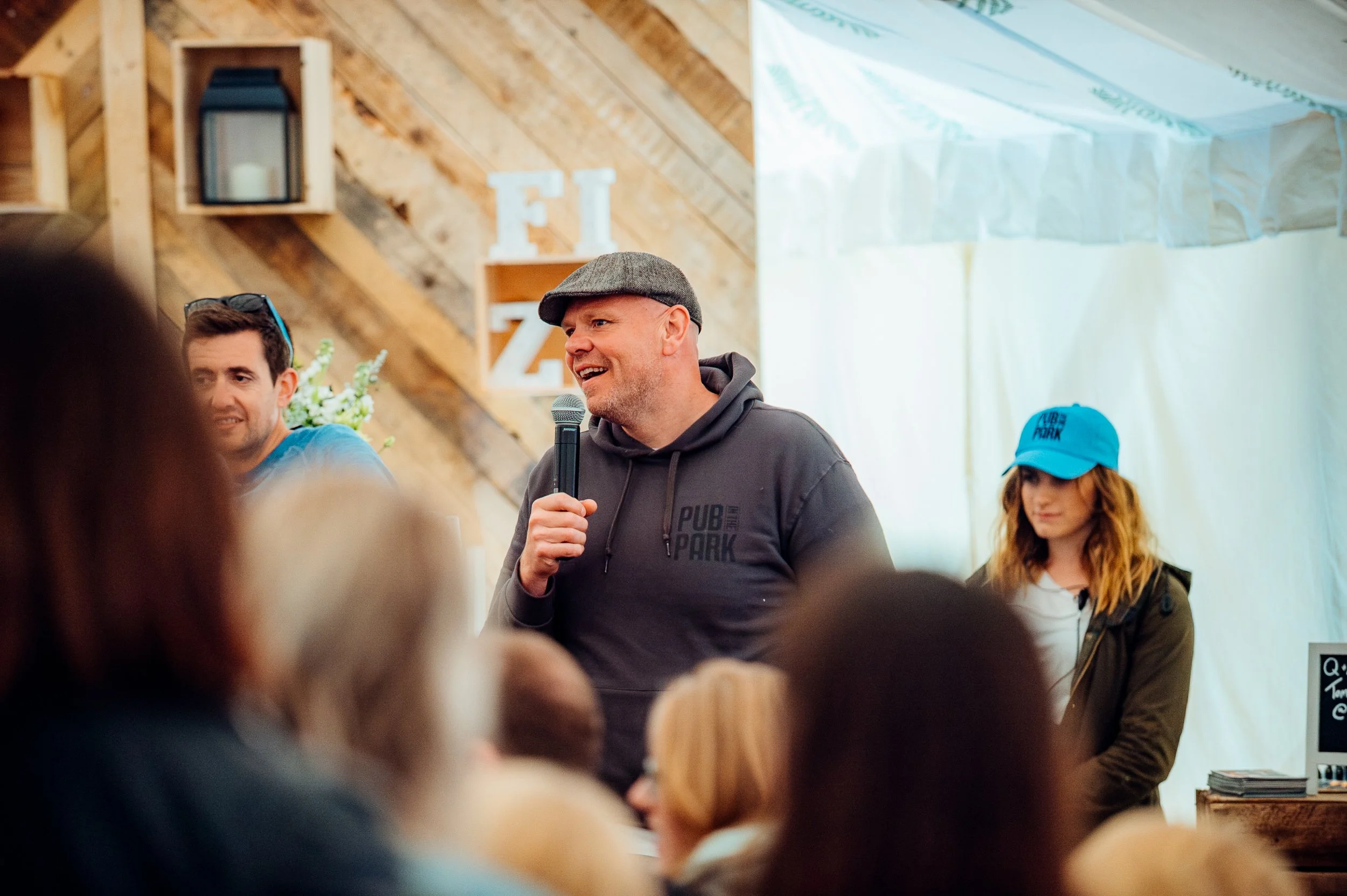 Celebrity chef Tom Kerridge addressing a live crowd from the microphone stage during the Pub in the Park food and music festival. High-profile culinary entertainment and public lifestyle festival photography by Will Bailey.