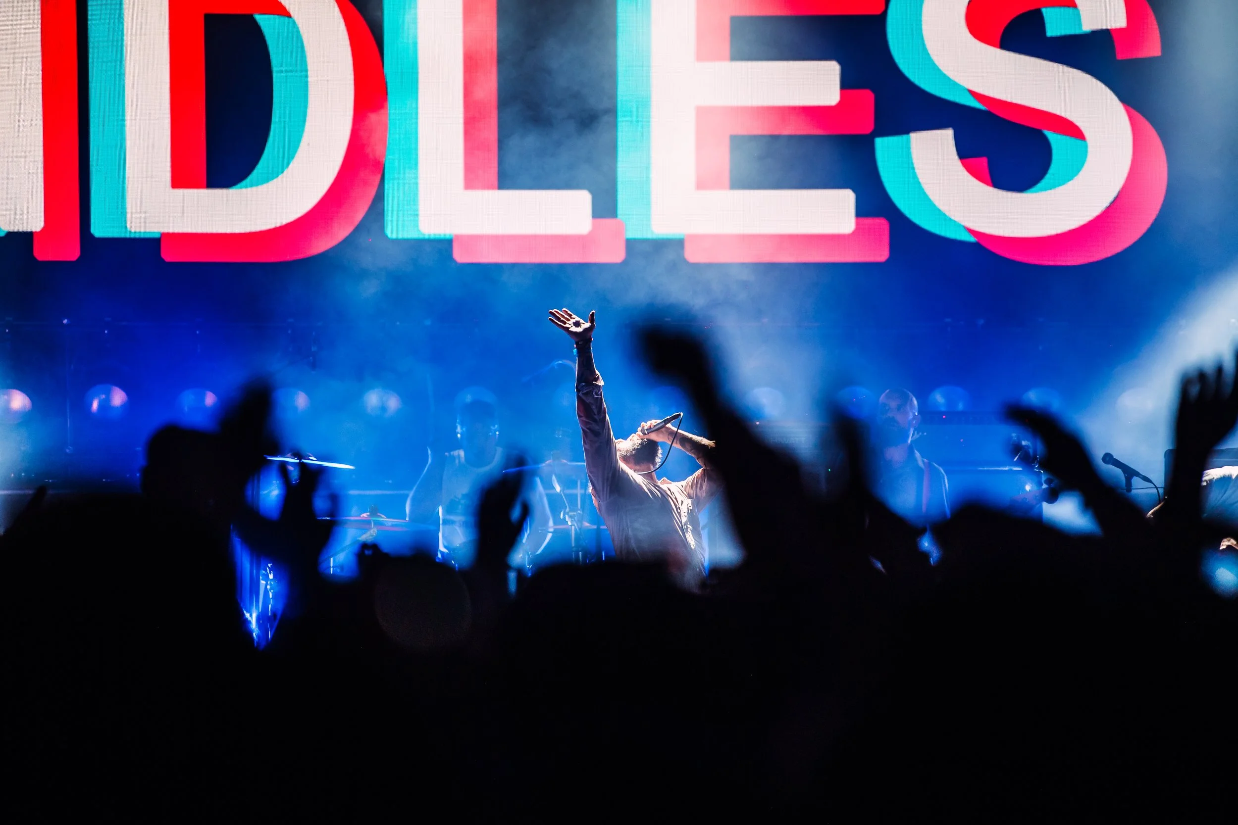 Lead singer Joe Talbot of IDLES performs in front of a giant neon band logo during a powerful headlining set at Boardmasters Festival in Cornwall. High-intensity punk rock concert and major music festival photography by Will Bailey.