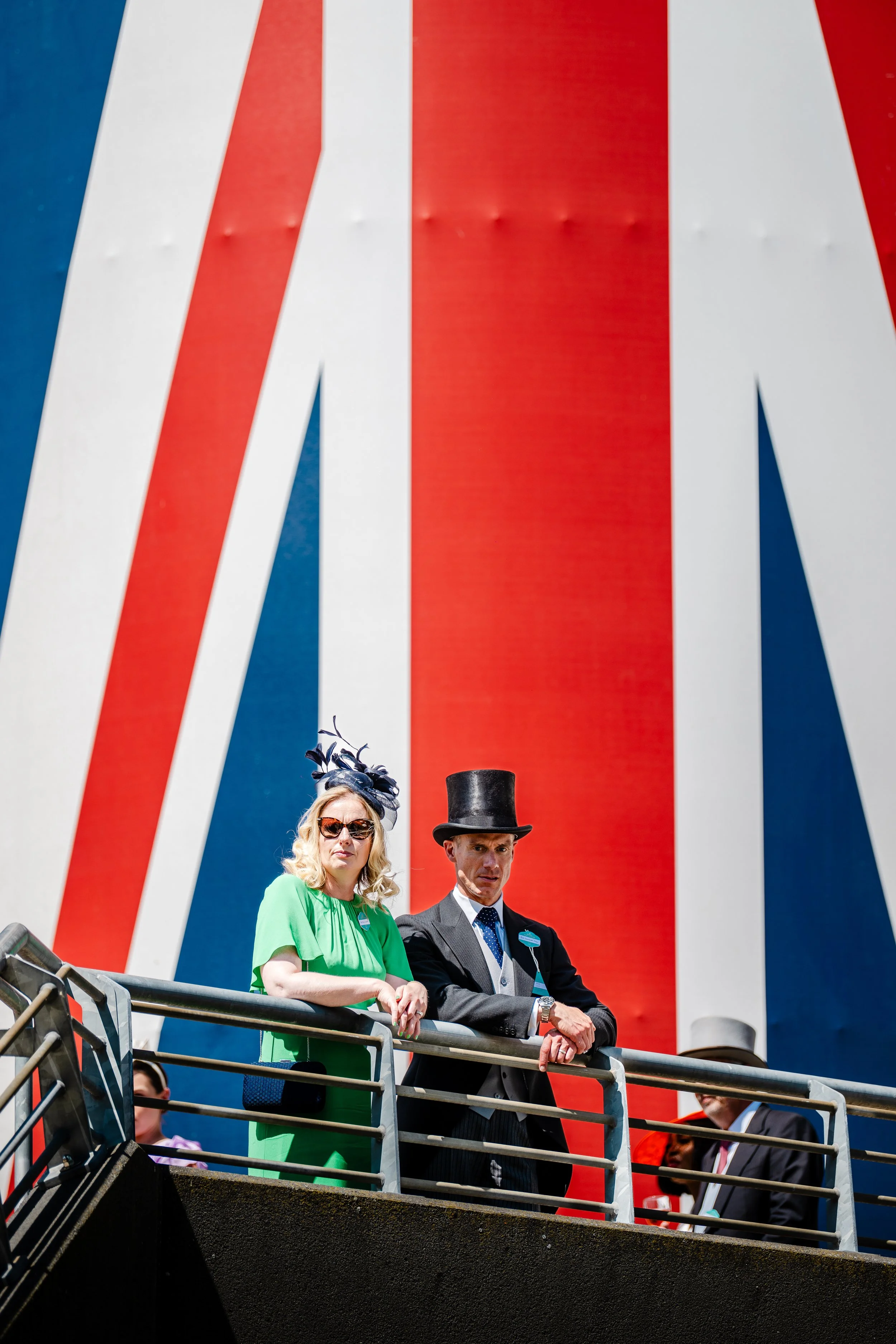 Spectators in morning dress overlooking the racecourse tracks against a vibrant backdrop at Ascot, Berkshire. High-society cultural tradition and premium sports event photography by Will Bailey.