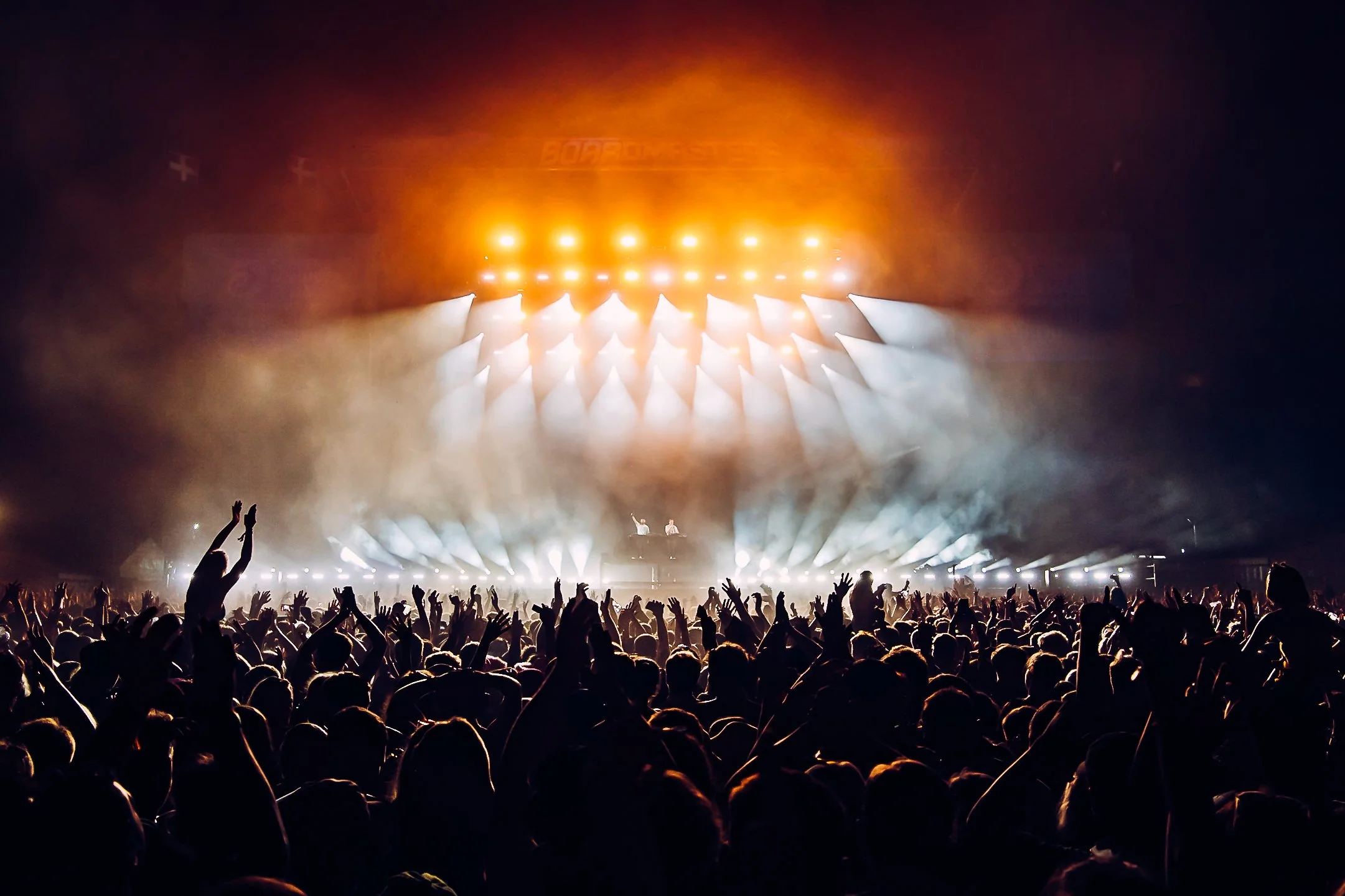 Wide festival photography of Disclosure at Boardmasters. A large crowd with hands raised against intense orange stage lighting. Photo by Will Bailey