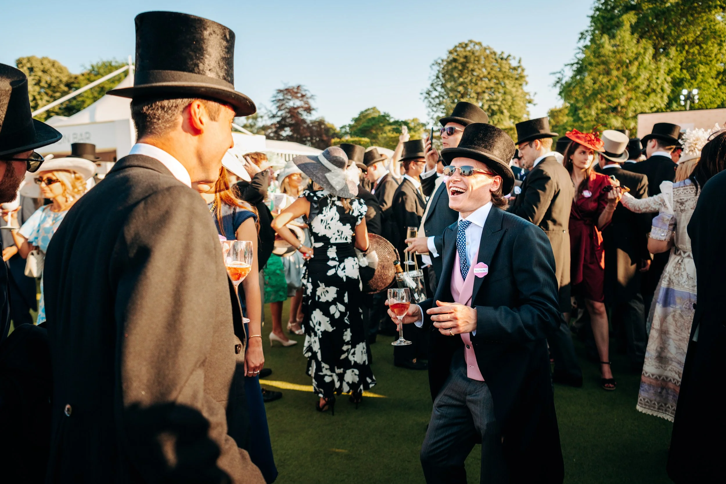 Candid laughter shared among guests in formal attire during an evening lawn reception at a luxury social calendar event in Berkshire. Premium summer season social lifestyle photography by Will Bailey.