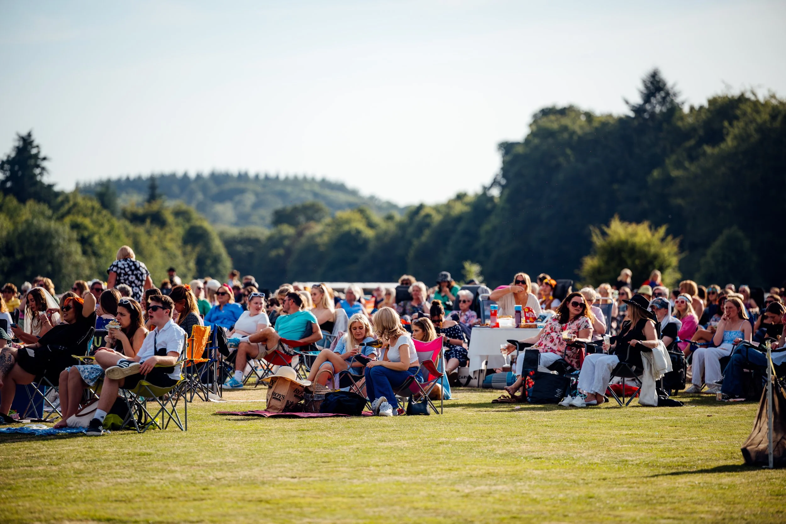 An outdoor audience relaxing in lawn chairs during a sunny afternoon screening with Adventure Cinema at Stansted Park on the Hampshire and West Sussex border. Premium country estate lifestyle and public entertainment photography by Will Bailey.
