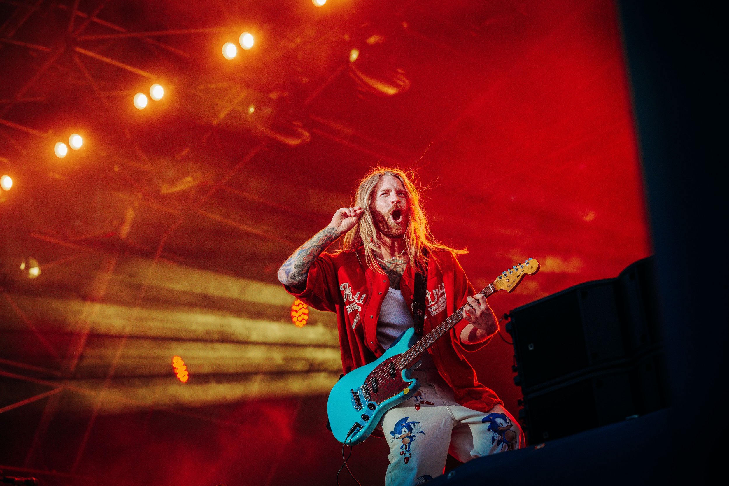 Singer Sam Ryder delivering a soaring vocal performance while playing a turquoise electric guitar under intense red stage wash at CarFest in Basingstoke, Hampshire. High-profile celebrity concert and professional music festival photography by Will Ba