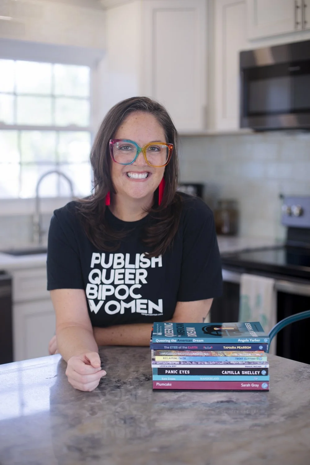 Rev. Dr. Angela Yarber, founder of Tehom Center Publishing, wearing a Publish Queer BIPOC Women t-shirt and holding books