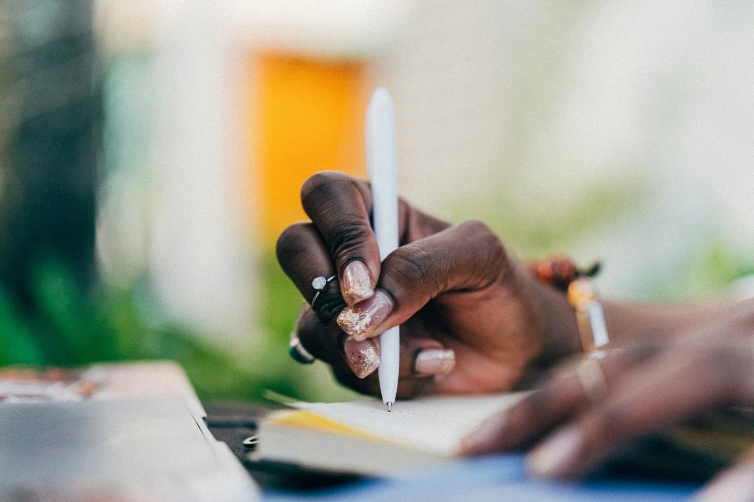 A person of color writing in a notebook with a stylus pen outdoors