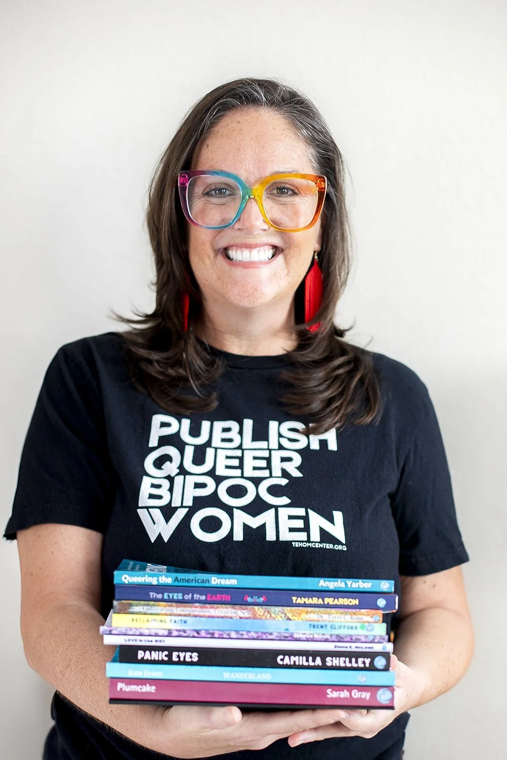 Angela Yarber, founder of Tehom Center Publishing, holding a stack of books