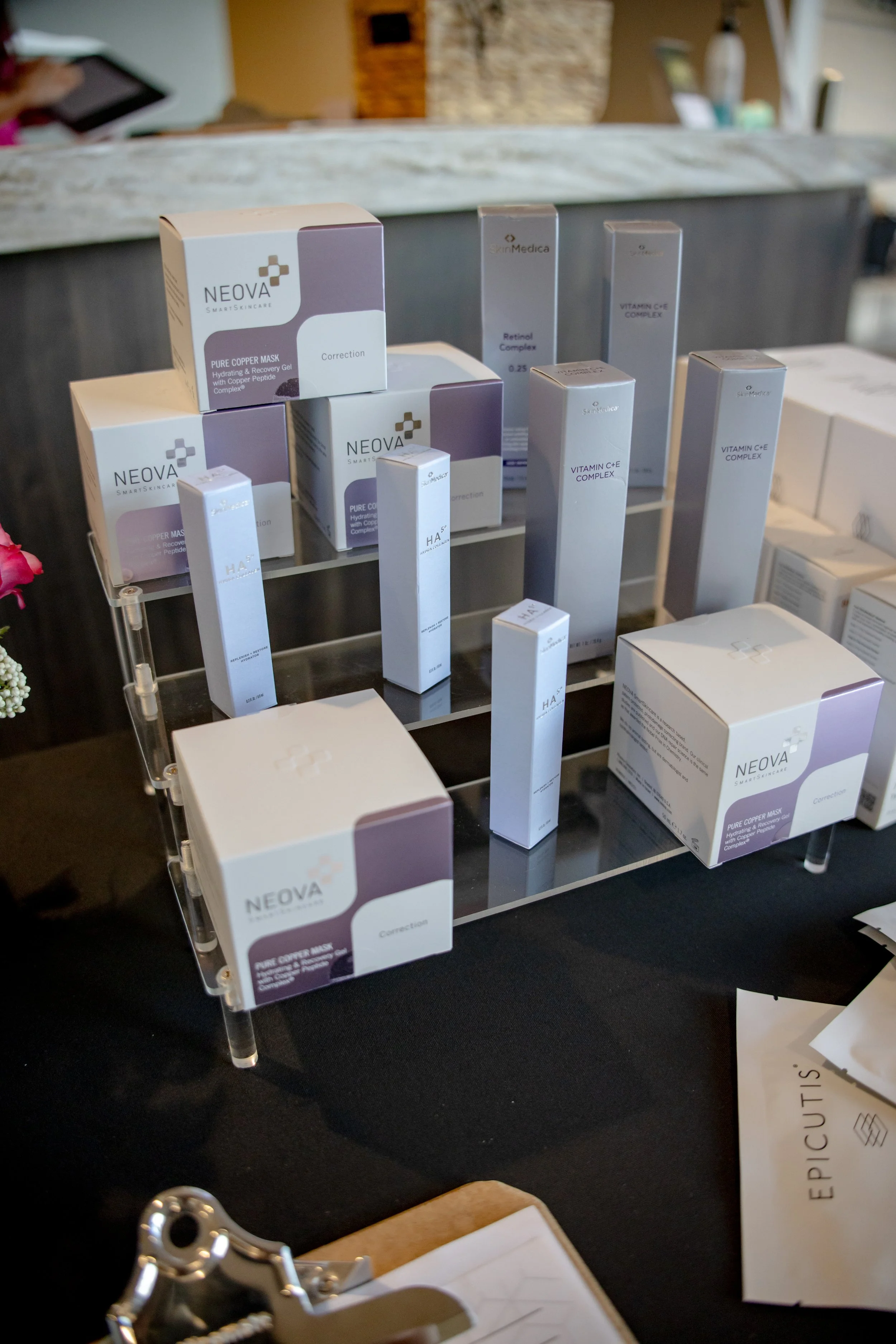 A display of skincare products on a multi-tiered stand, including boxes labeled NEOVA and SkinMedica, on a black countertop.