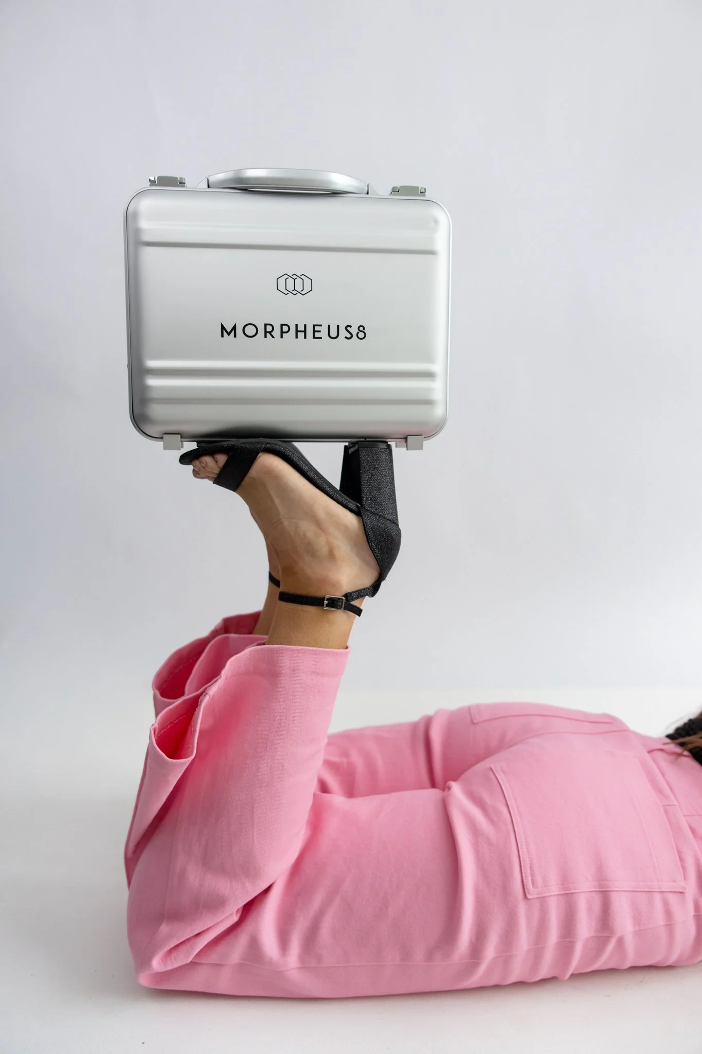 Person wearing a pink sweatshirt and holding a silver metal case with the Morpheus logo against a plain light background.