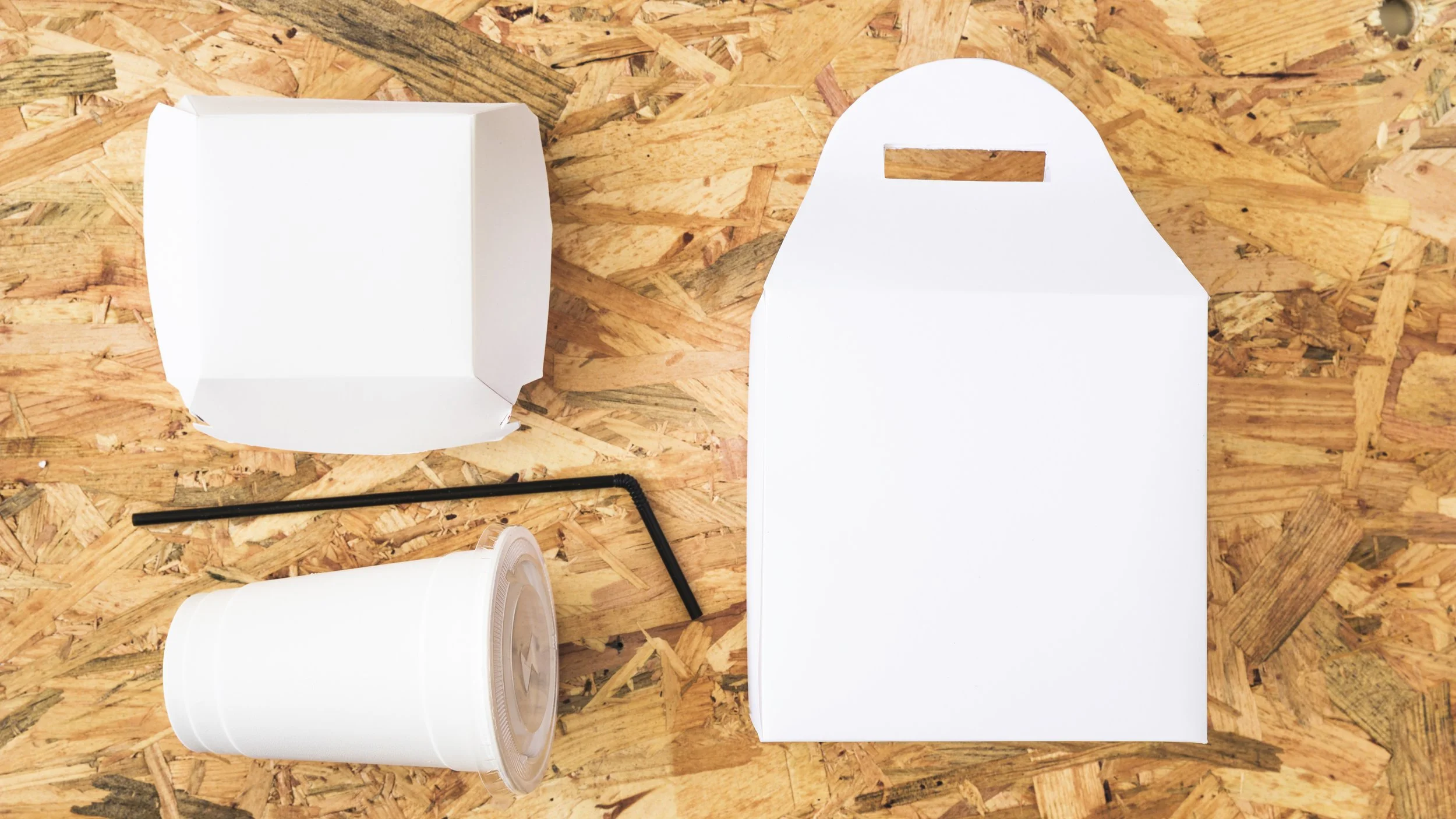 White paper food takeout containers and black straws placed on a wooden surface.