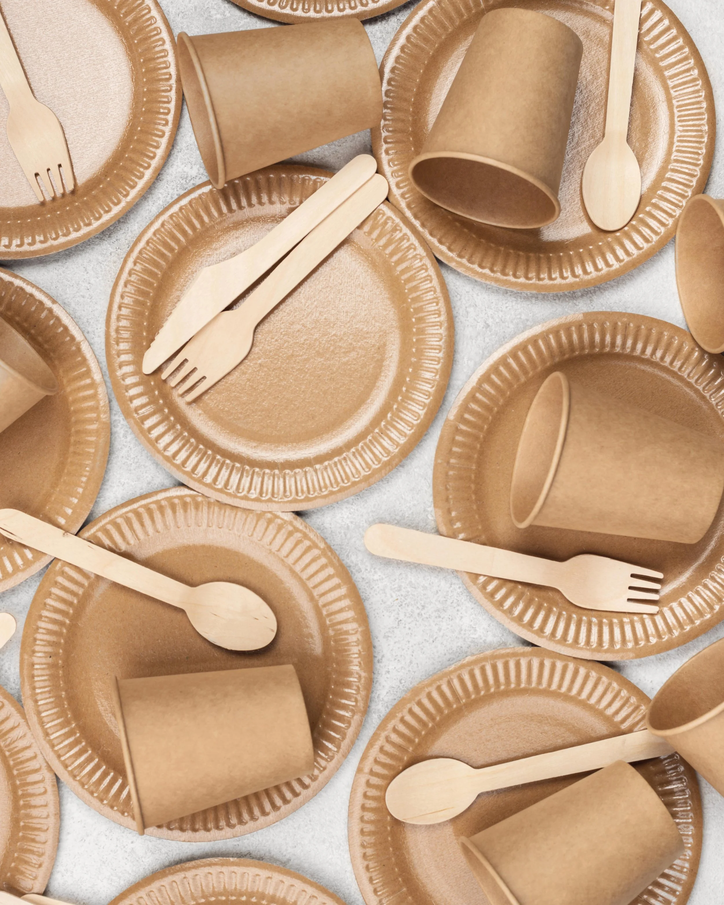 Disposable brown paper plates, cups, and wooden utensils arranged on a white surface, likely for a takeout or picnic meal.