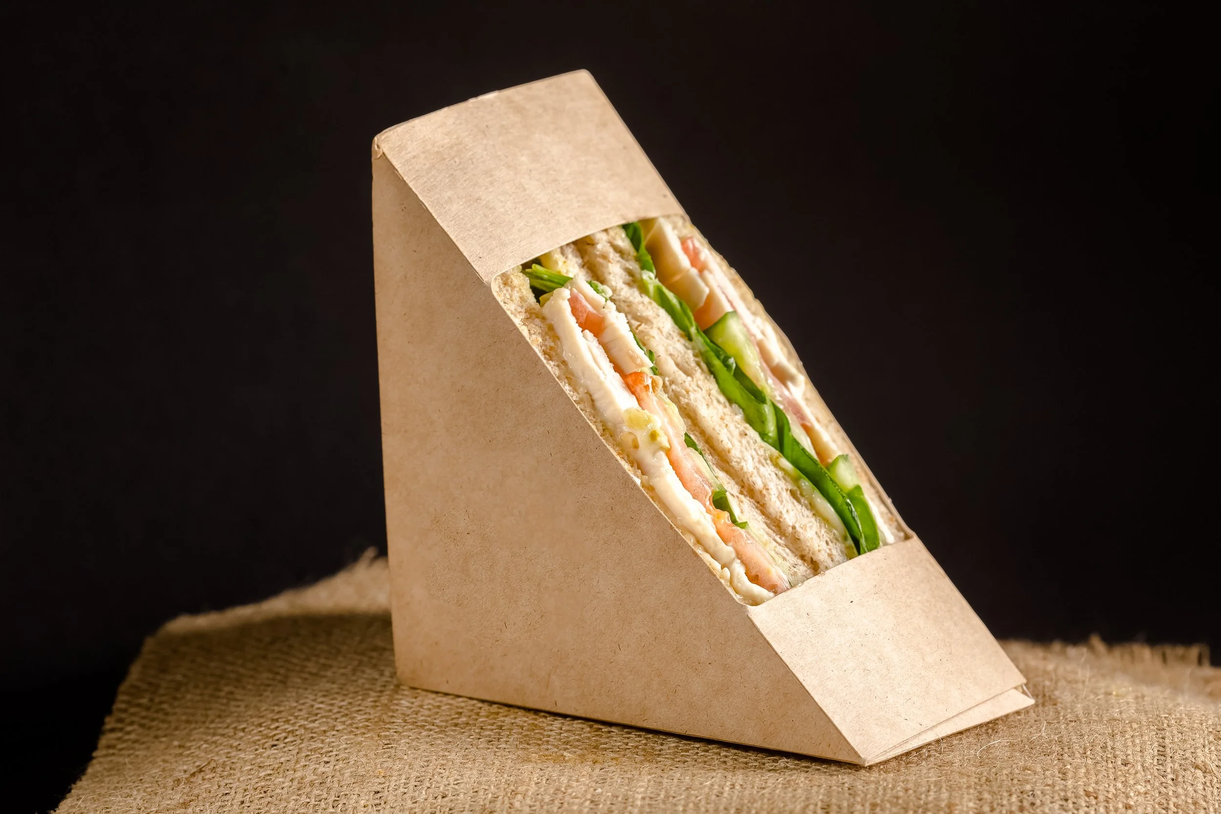 Sandwich with lettuce, tomato, cheese, and turkey inside a paper wrap, sitting on a textured surface.