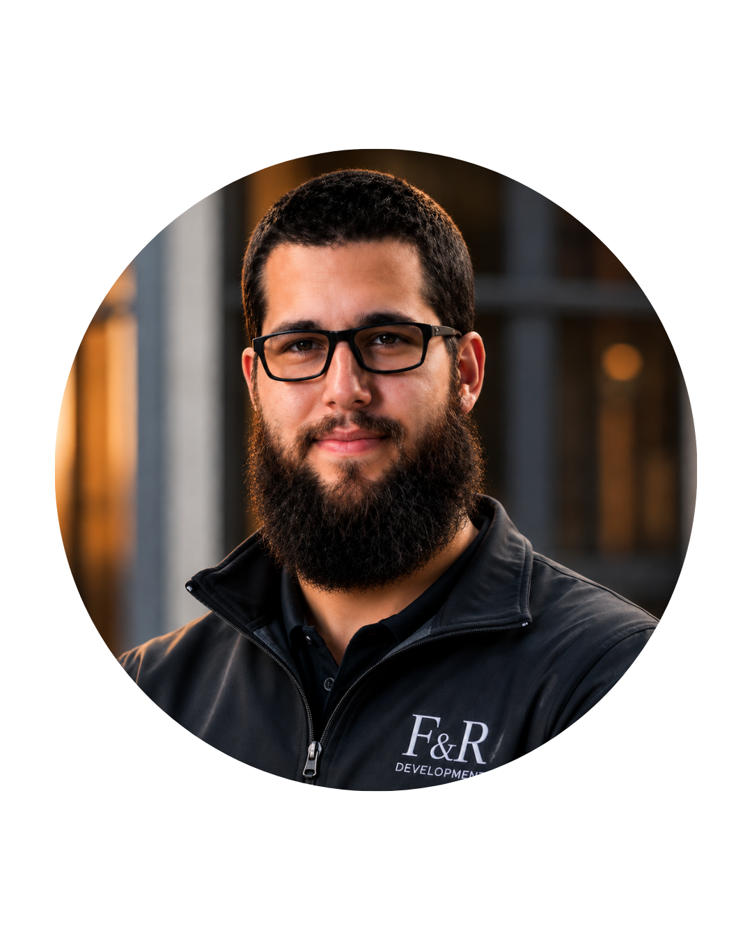 Headshot of a bearded man wearing glasses and a black F&R Development jacket, standing outdoors with blurred building in background.