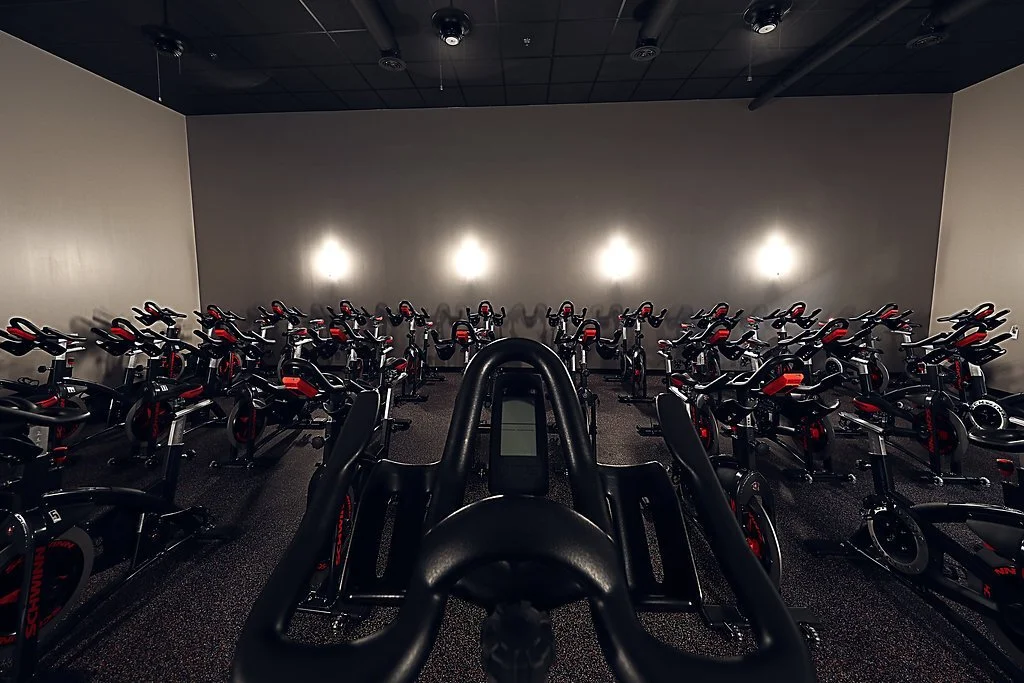 A gym room filled with stationary exercise bikes arranged in rows.