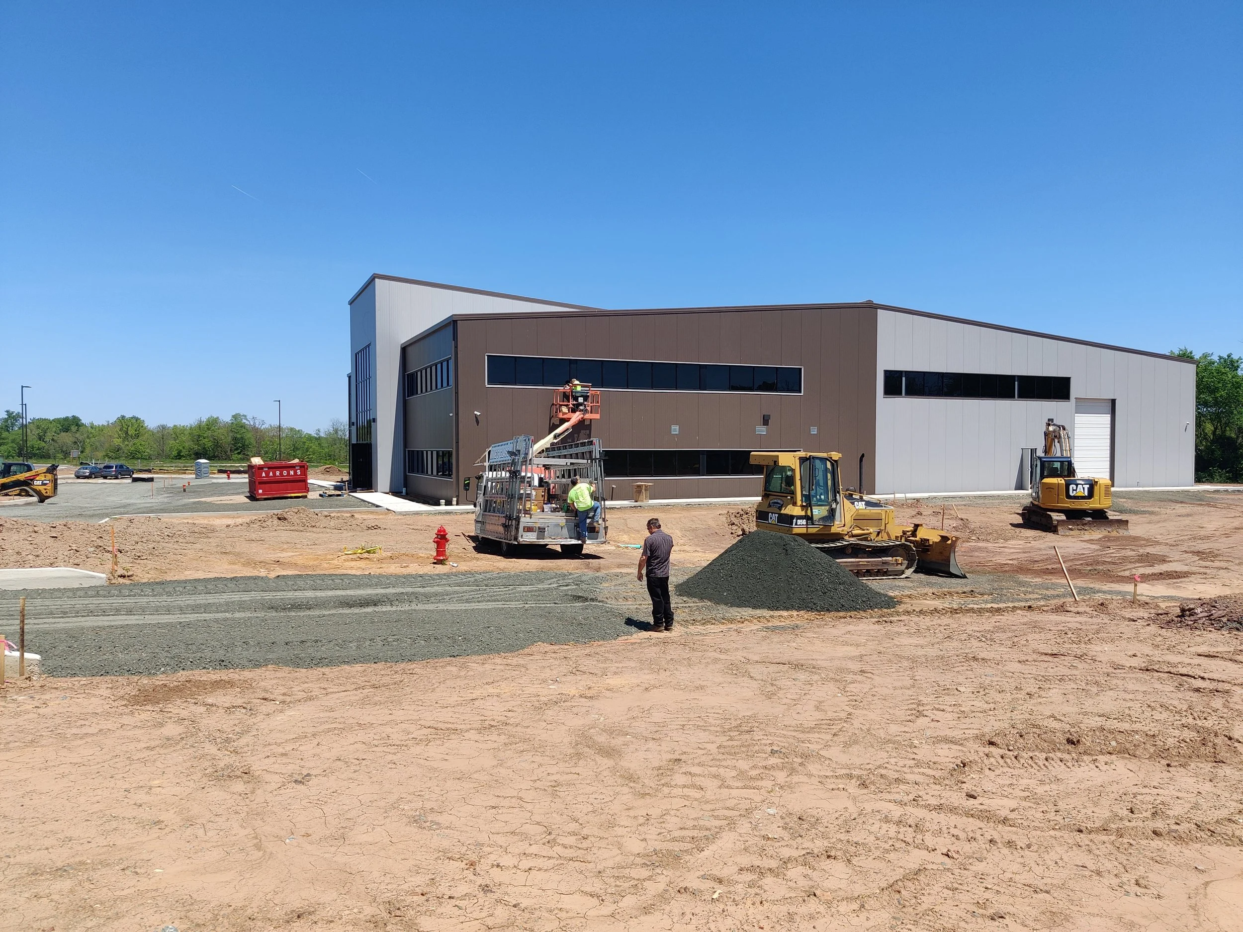 Construction site with a modern building under construction, machinery, and workers working on the site under a clear blue sky.
