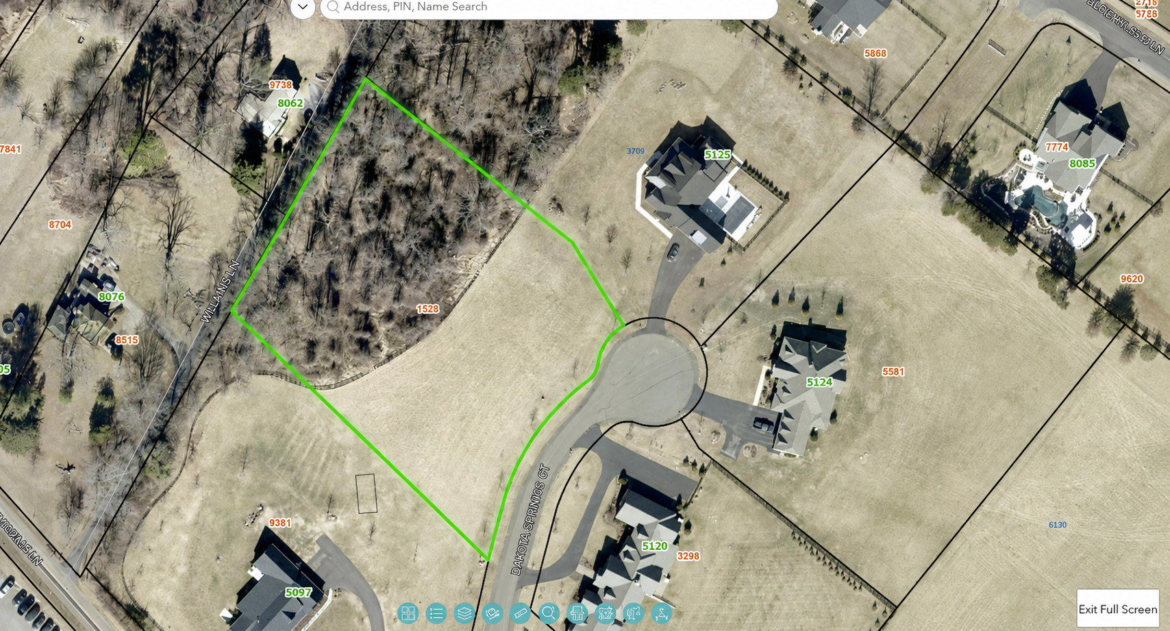 Aerial view of a residential neighborhood featuring several houses, lawns, trees, and a vacant wooded lot outlined in green, located along Dakota Springs Ct and Williams Ln.