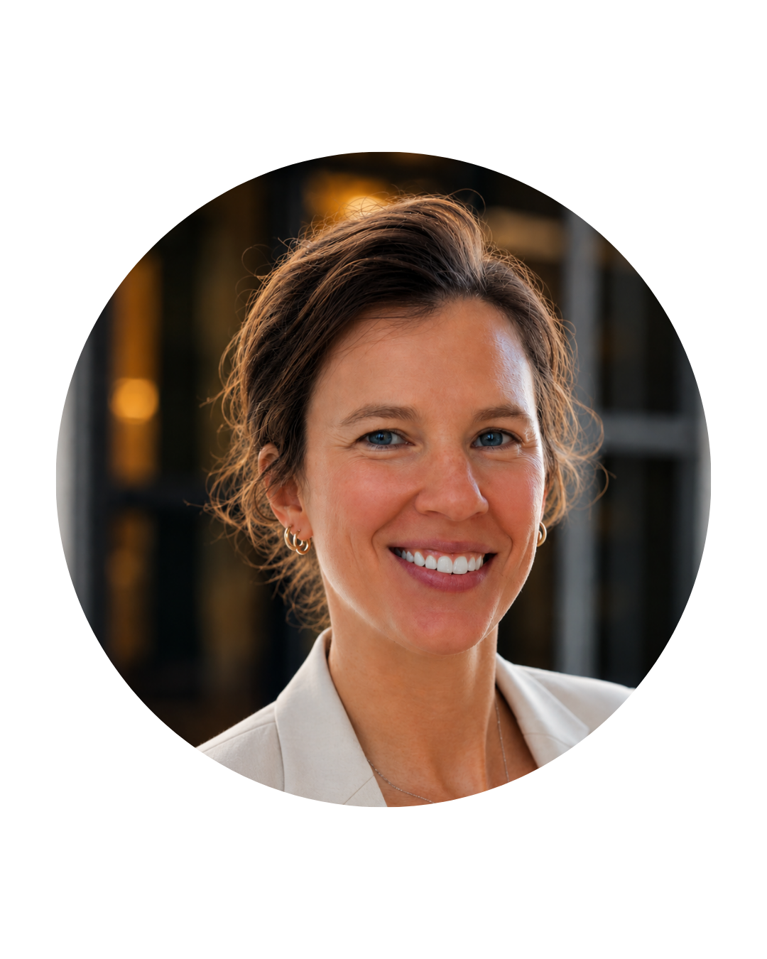 Portrait of a smiling woman with short brown hair, blue eyes, wearing earrings, and a light-colored blazer.