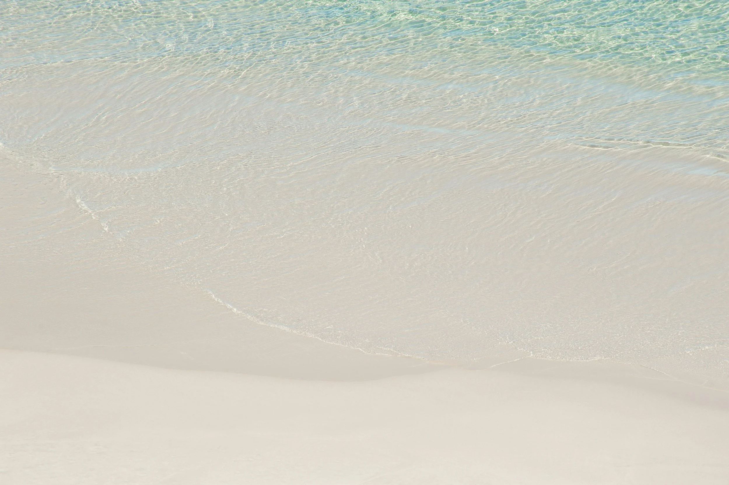 Gentle waves washing onto a sandy beach with clear, turquoise water.