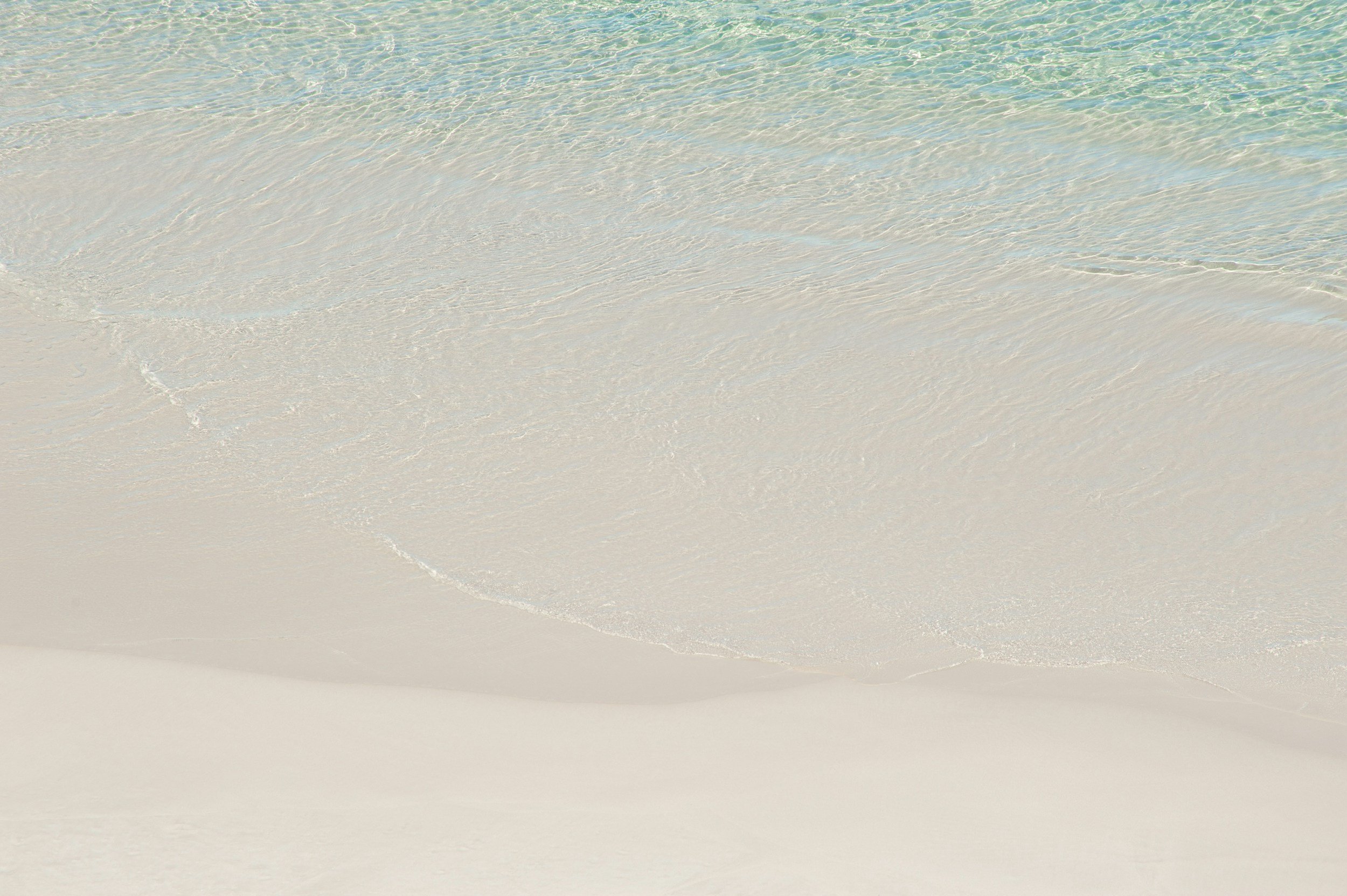 Photo of clear ocean water gently washing onto a white sandy beach.