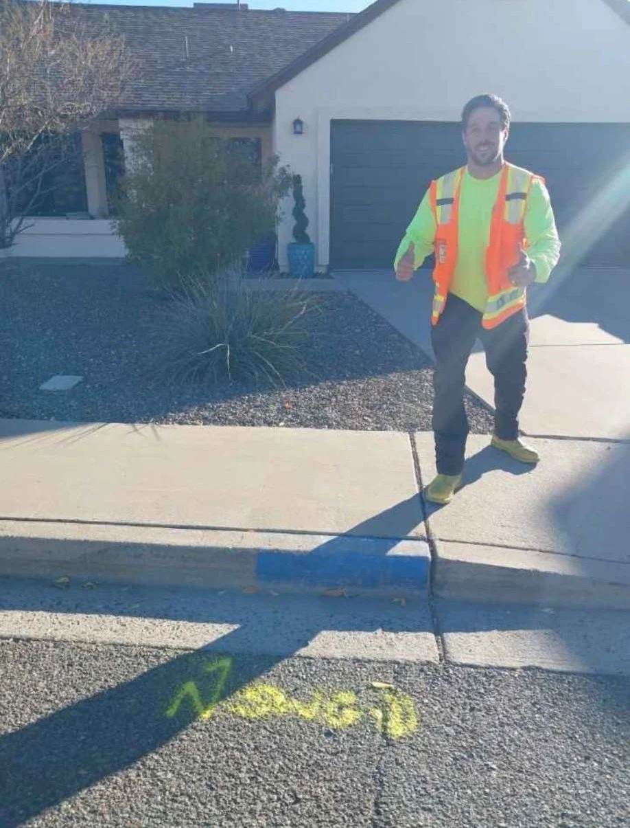 A man in a neon yellow shirt and orange safety vest jogging on a residential sidewalk in front of a house with a garage. The man is smiling and giving a thumbs-up, with the words 'NO PARKING' painted on the street in yellow.