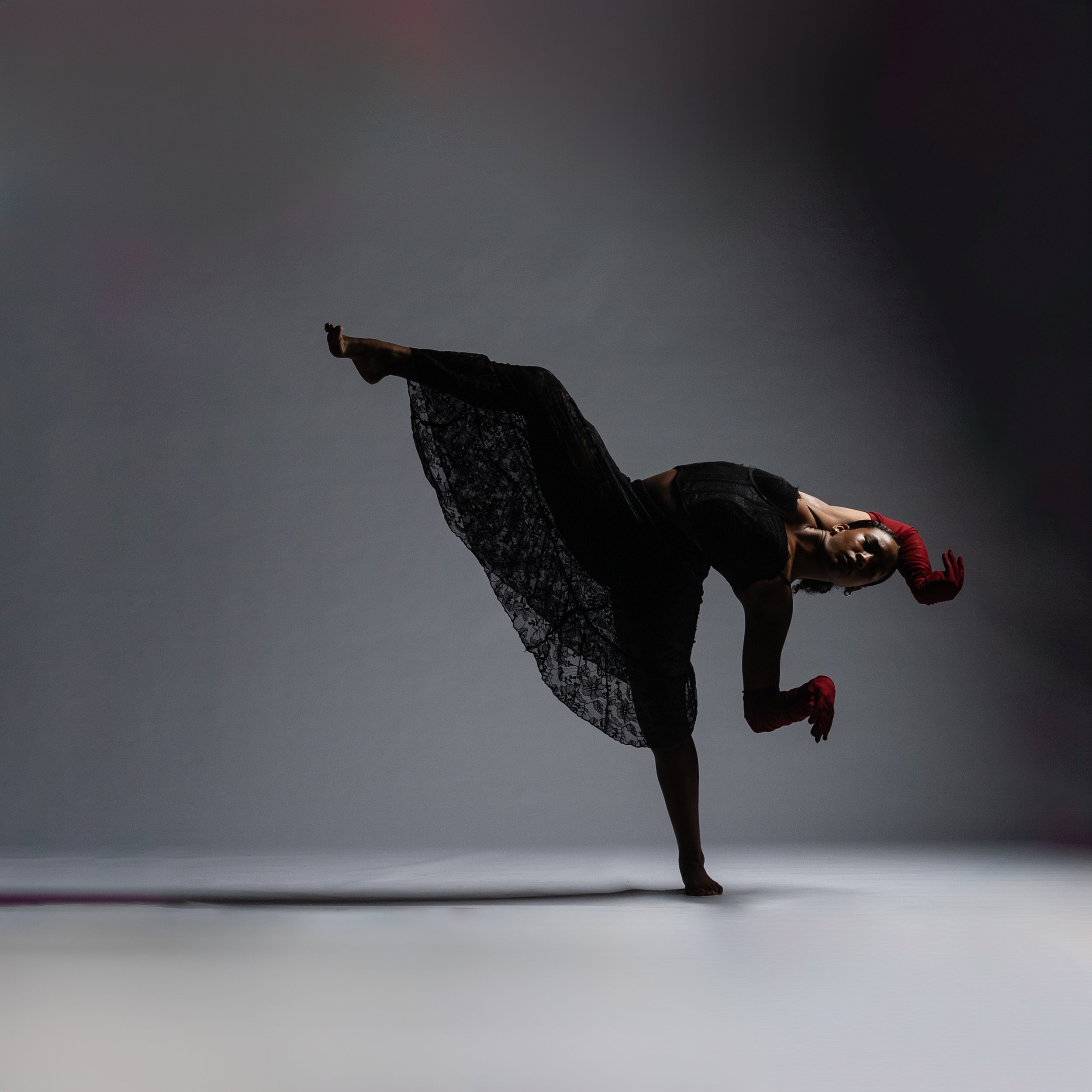 A woman performing a balanced yoga pose called Natarajasana or Lord of the Dance pose against a plain background. She is standing on one leg with her other leg bent backward and her foot held with her hand, while her other arm is extended forward.