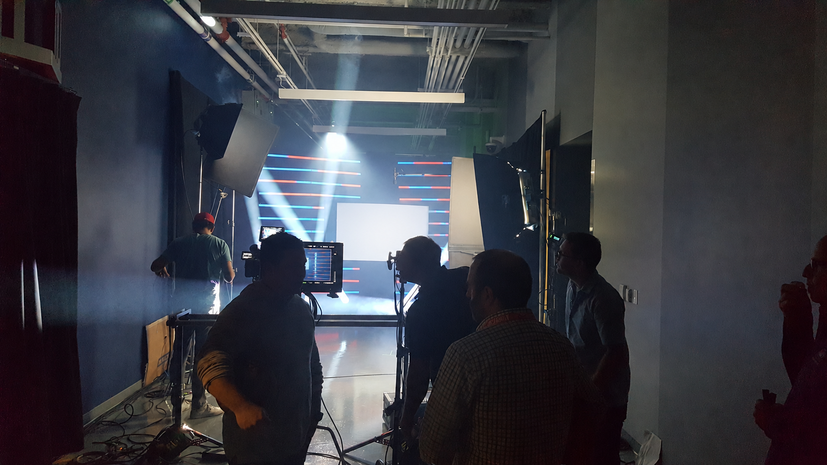 Behind-the-scenes view of a stage setup with lighting and screens, with crew members working and adjusting equipment in a dark room.
