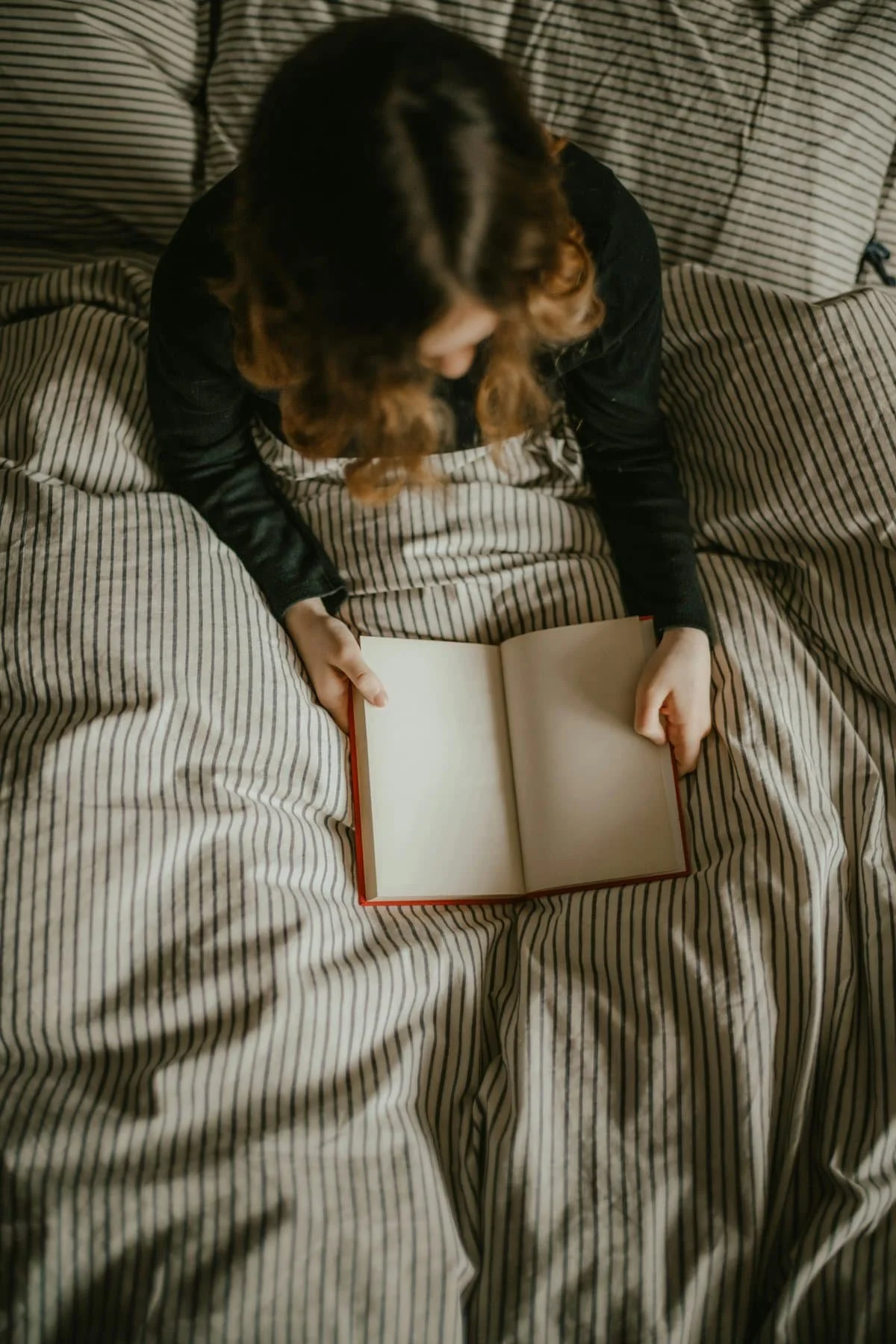 Person sitting on bed with striped bedding, looking at an open blank book.