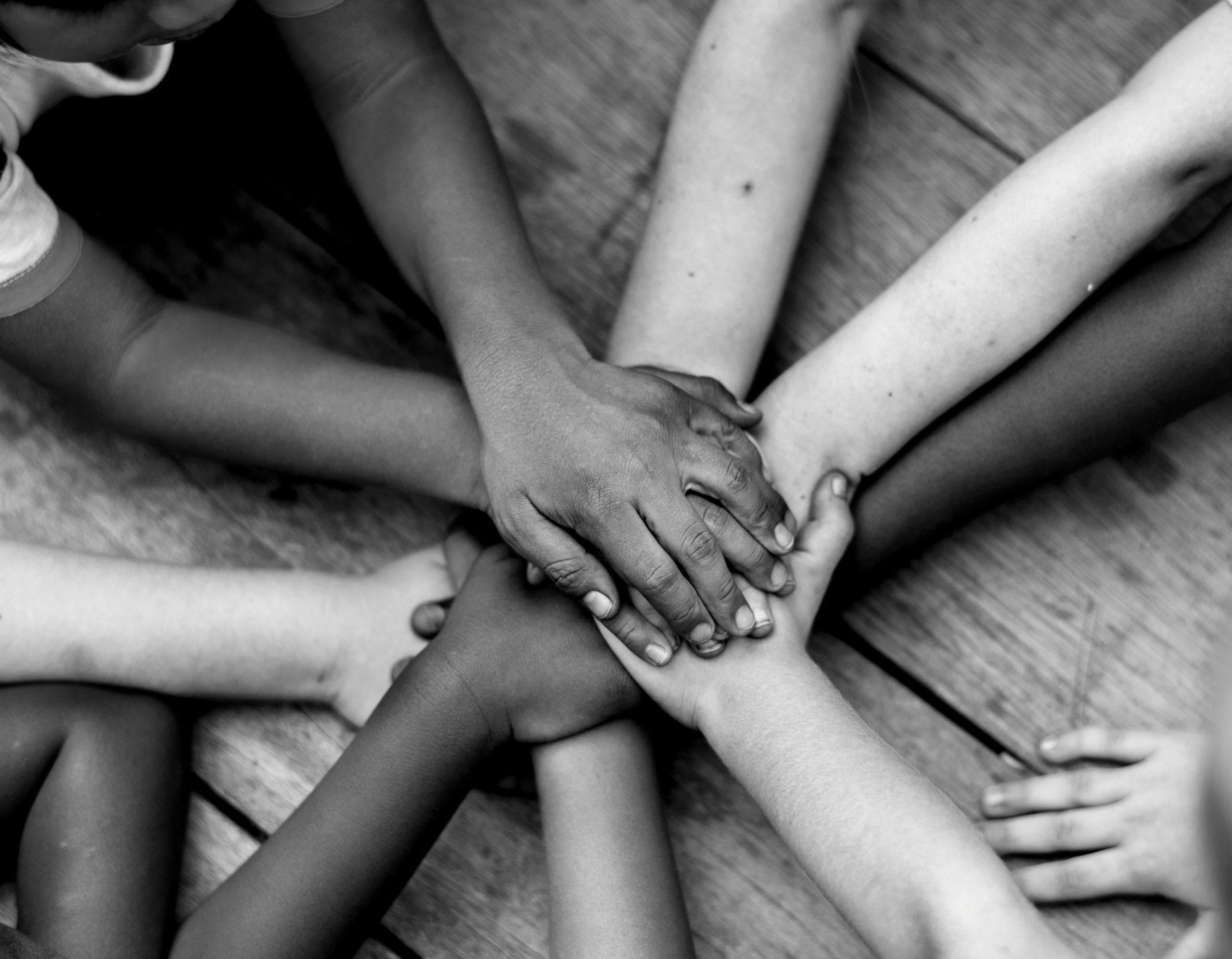 Multiple hands of different skin tones stacked together in a circle.